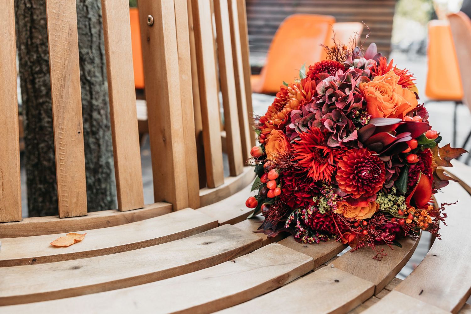 Vibrant autumn wedding bouquet with red, orange, and burgundy flowers resting on a wooden bench.