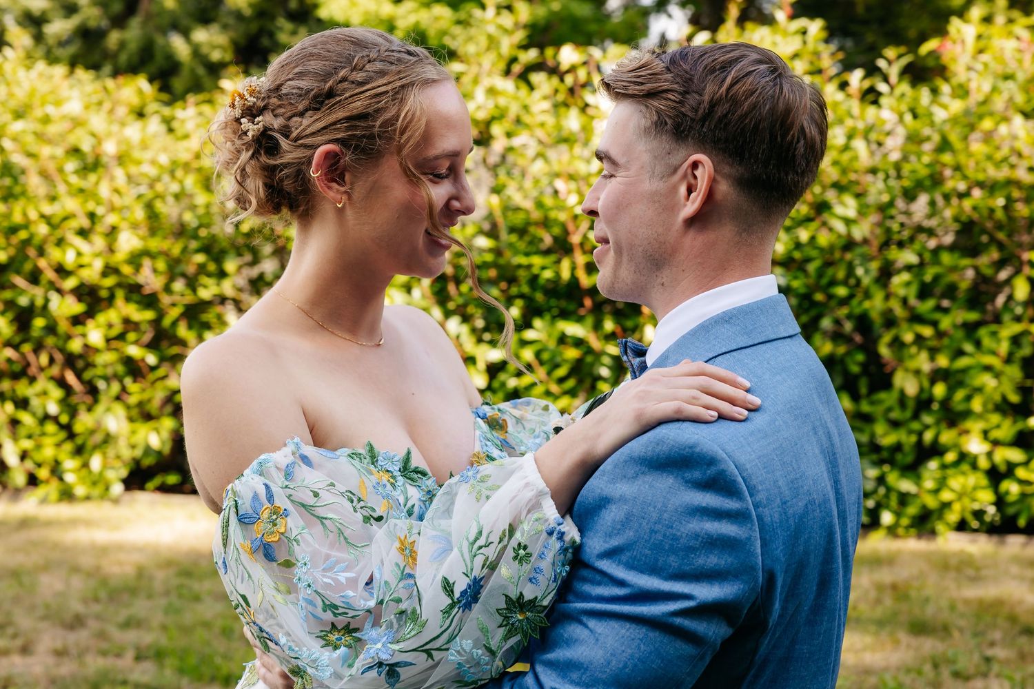 Bride and groom share an intimate gaze while embracing in a lush green garden setting.