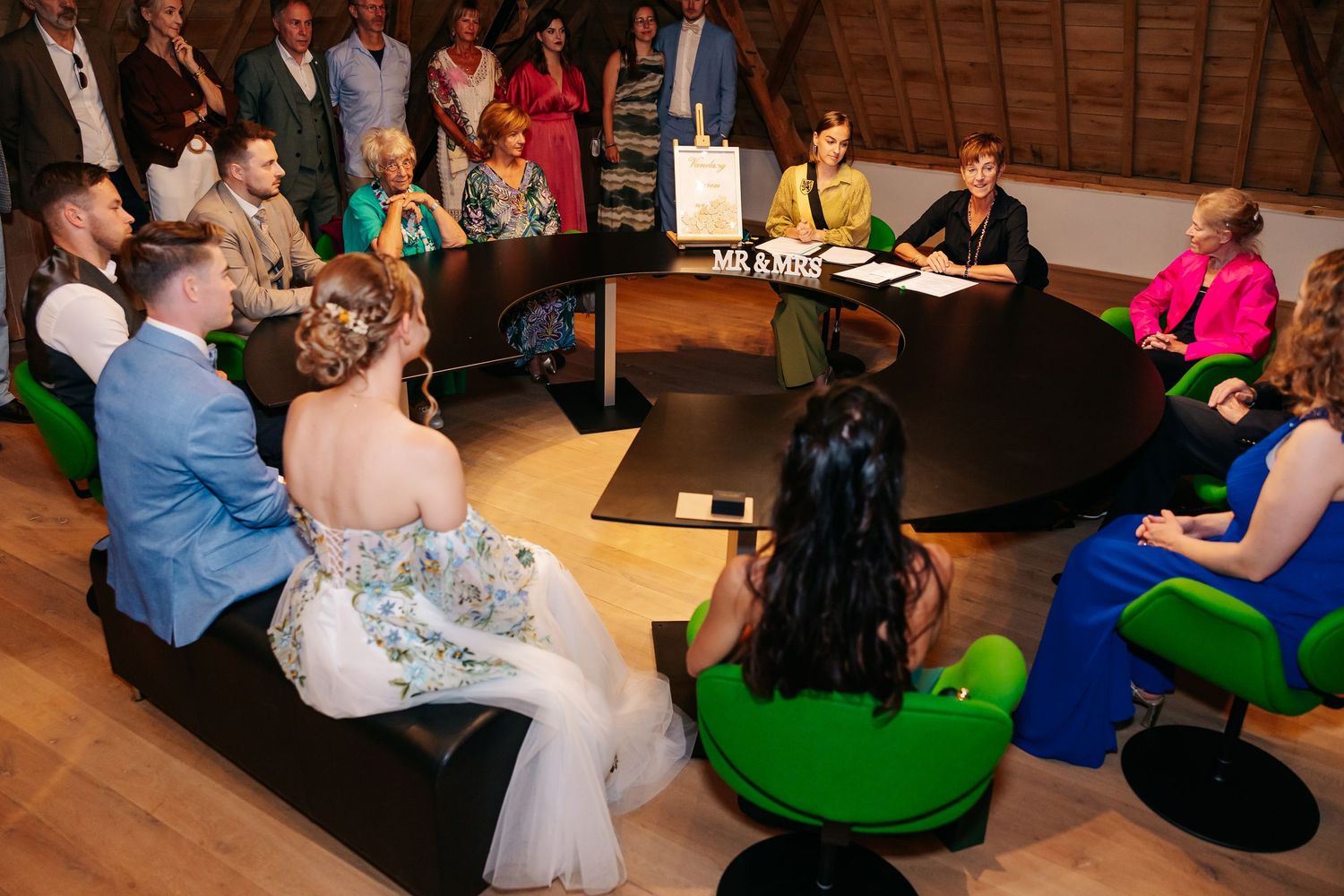 Wedding guests seated in circle around couple during intimate indoor marriage ceremony.