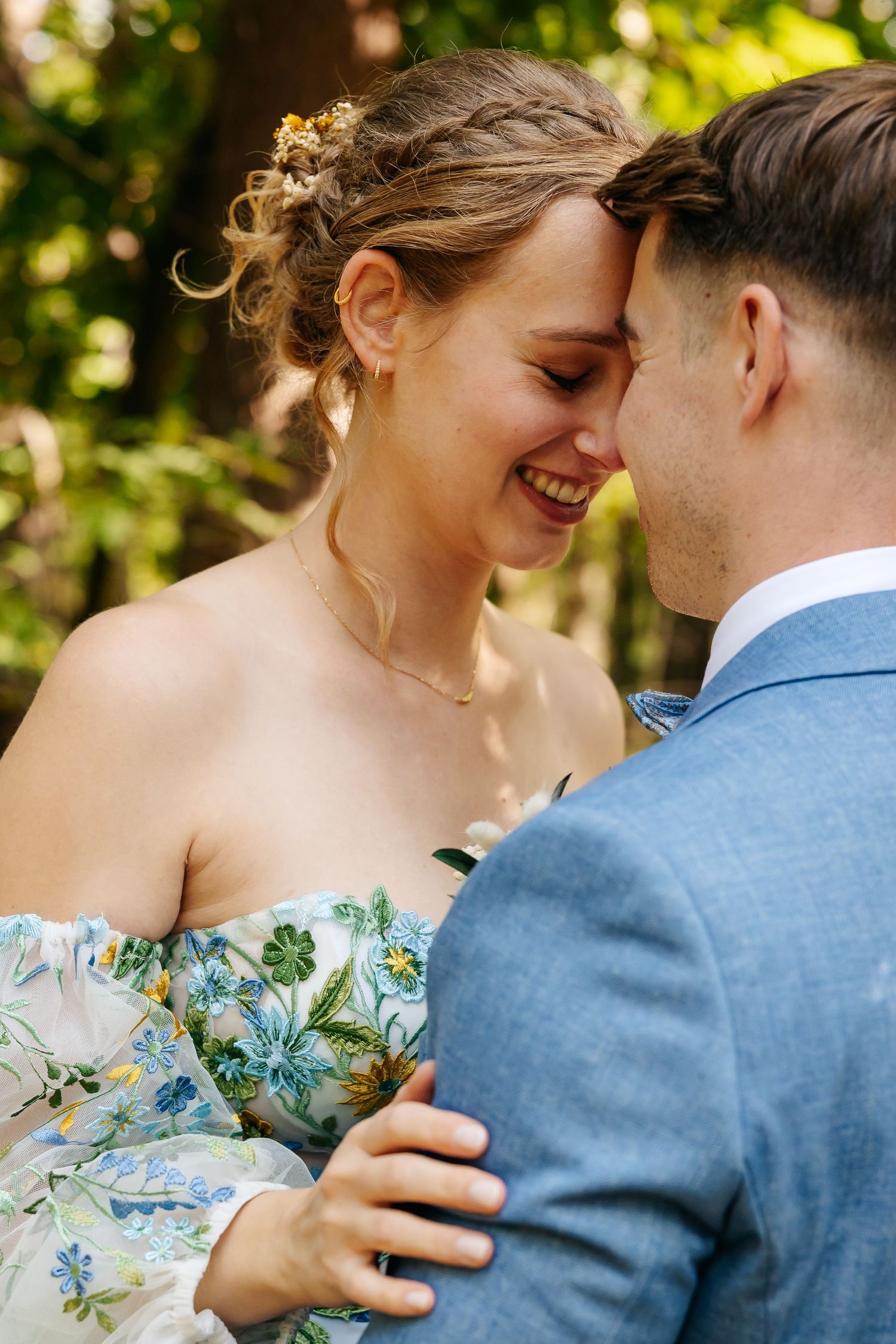 Laughing bride in floral dress touching foreheads with groom outdoors.