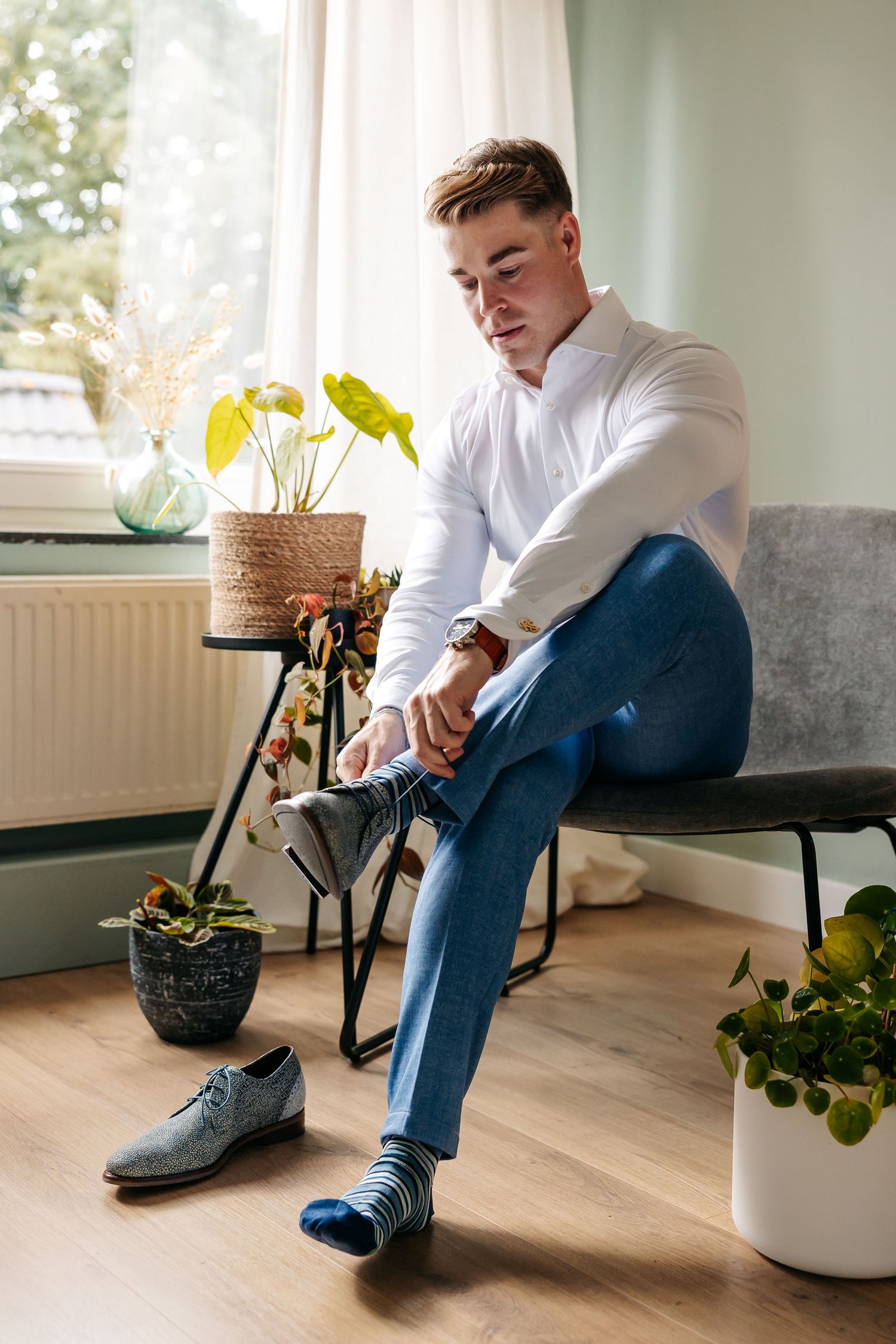 Groom in white shirt and blue pants putting on socks before wedding ceremony.