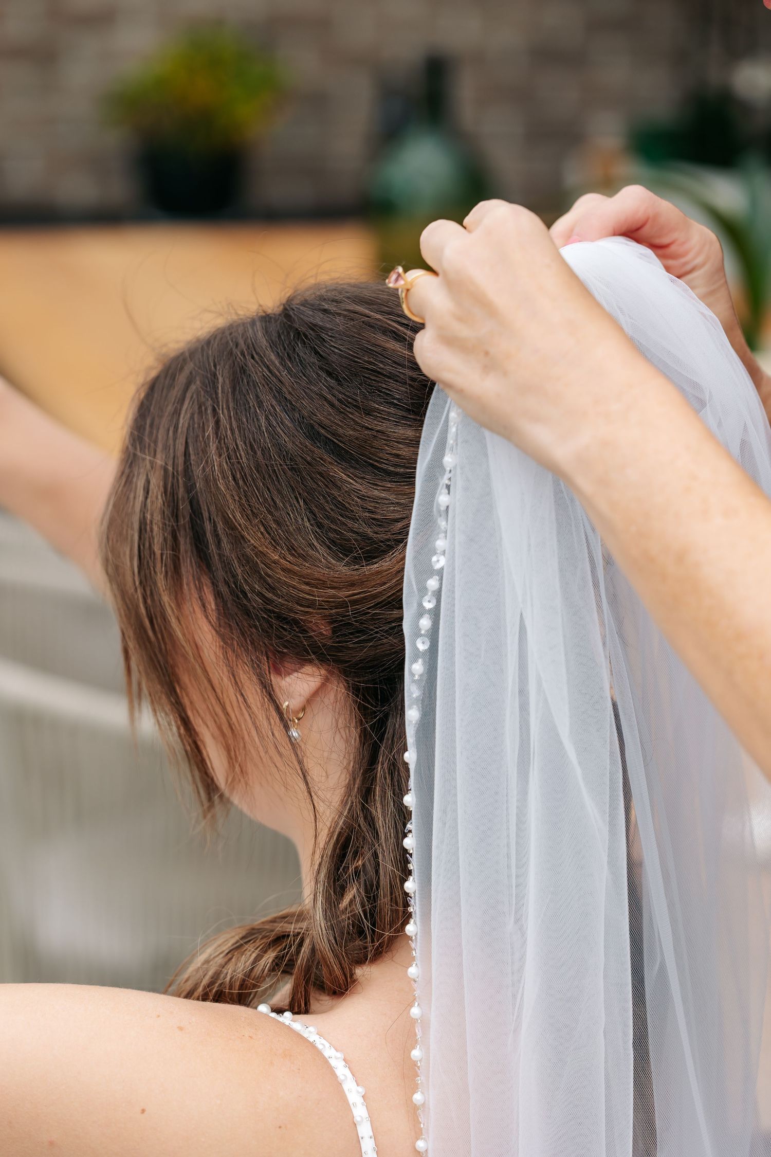 A helping hand pins a delicate pearl-trimmed veil into the bride's upswept brunette hair.