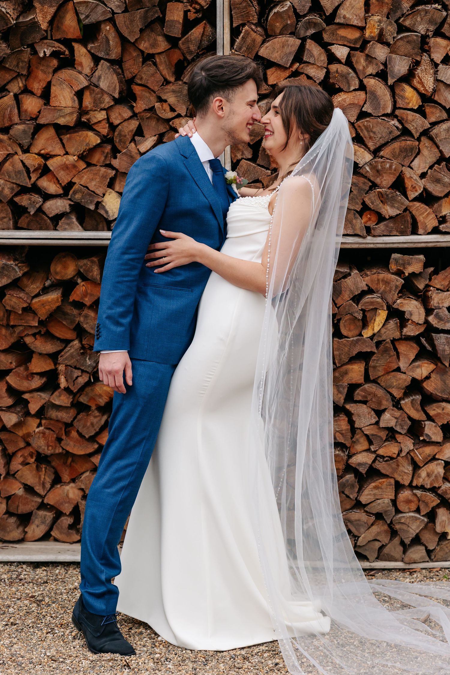 Bride and groom in blue suit sharing an intimate nose-to-nose moment before a stacked wood wall.