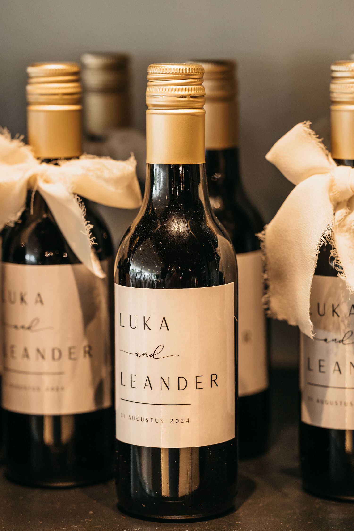 Custom wedding favor wine bottle labeled Luka and Leander with gold cap and linen ribbon.