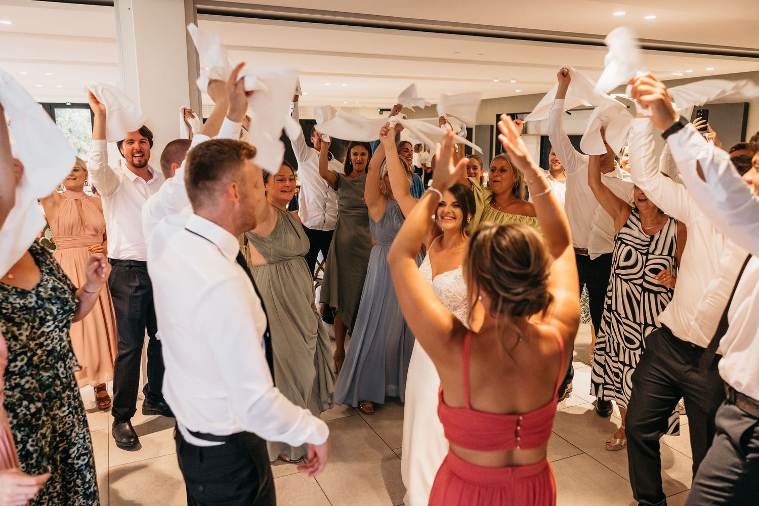Joyful wedding reception dance floor with guests waving white napkins.