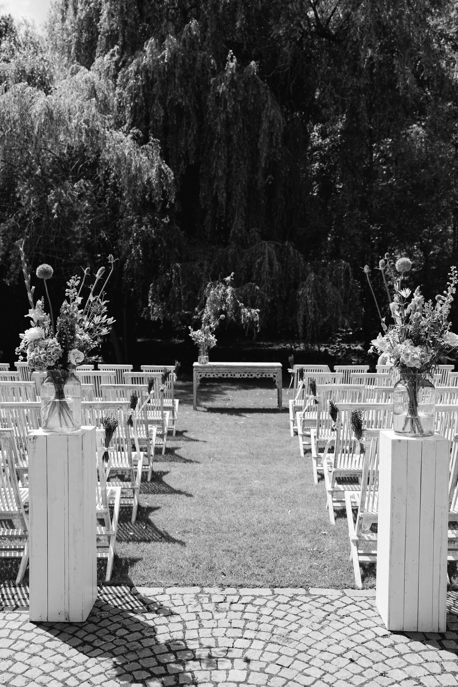 Black and white outdoor wedding ceremony setup with white chairs and floral arrangements.