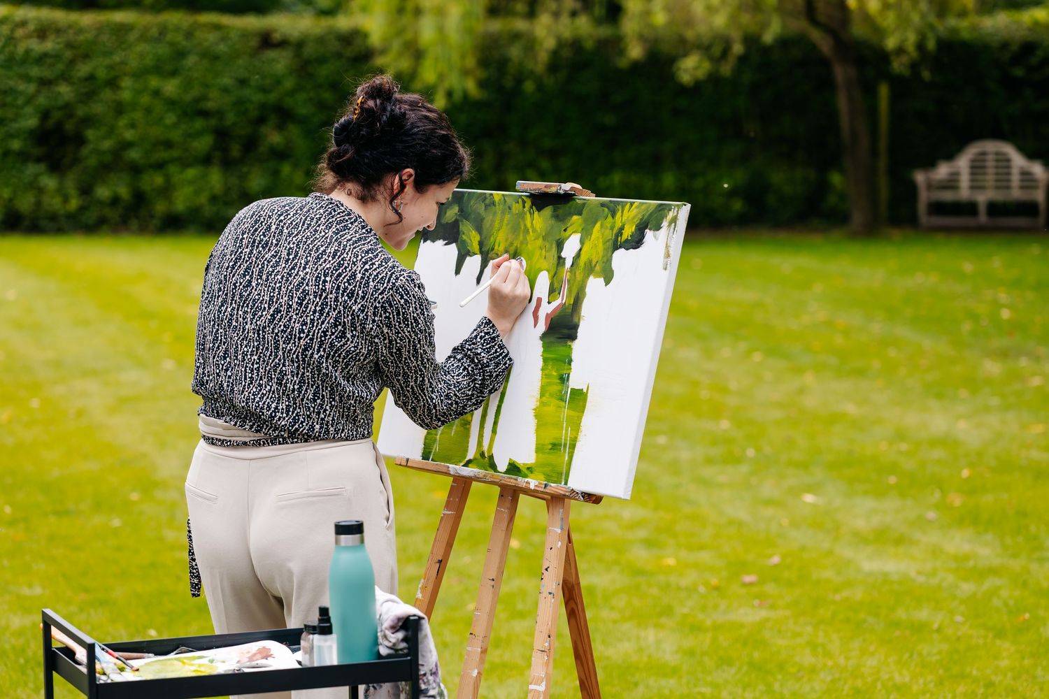 Artist painting a wedding scene on canvas at an easel in a sunny green garden.