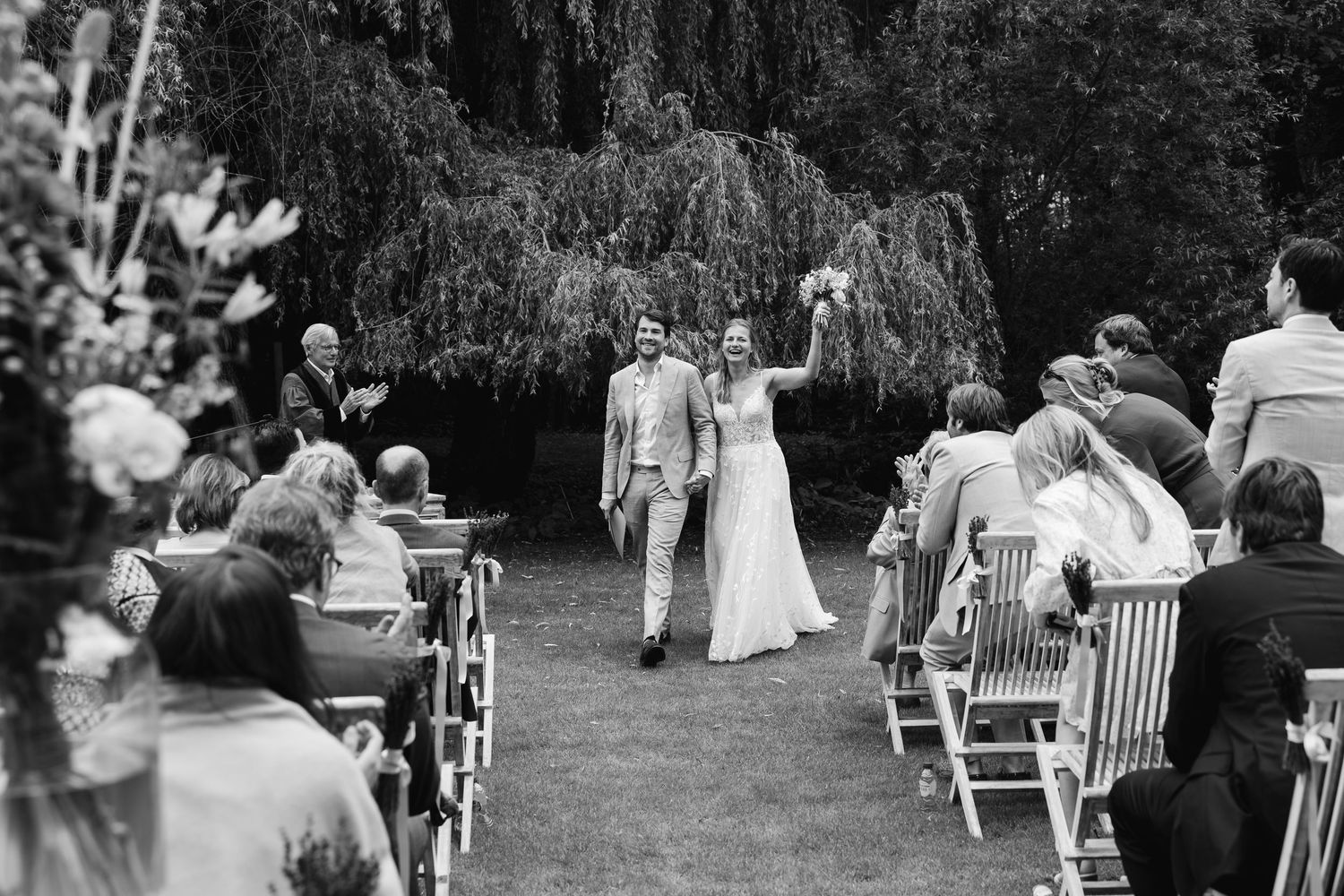 Black and white photo of newlyweds celebrating walk down aisle at outdoor garden wedding.