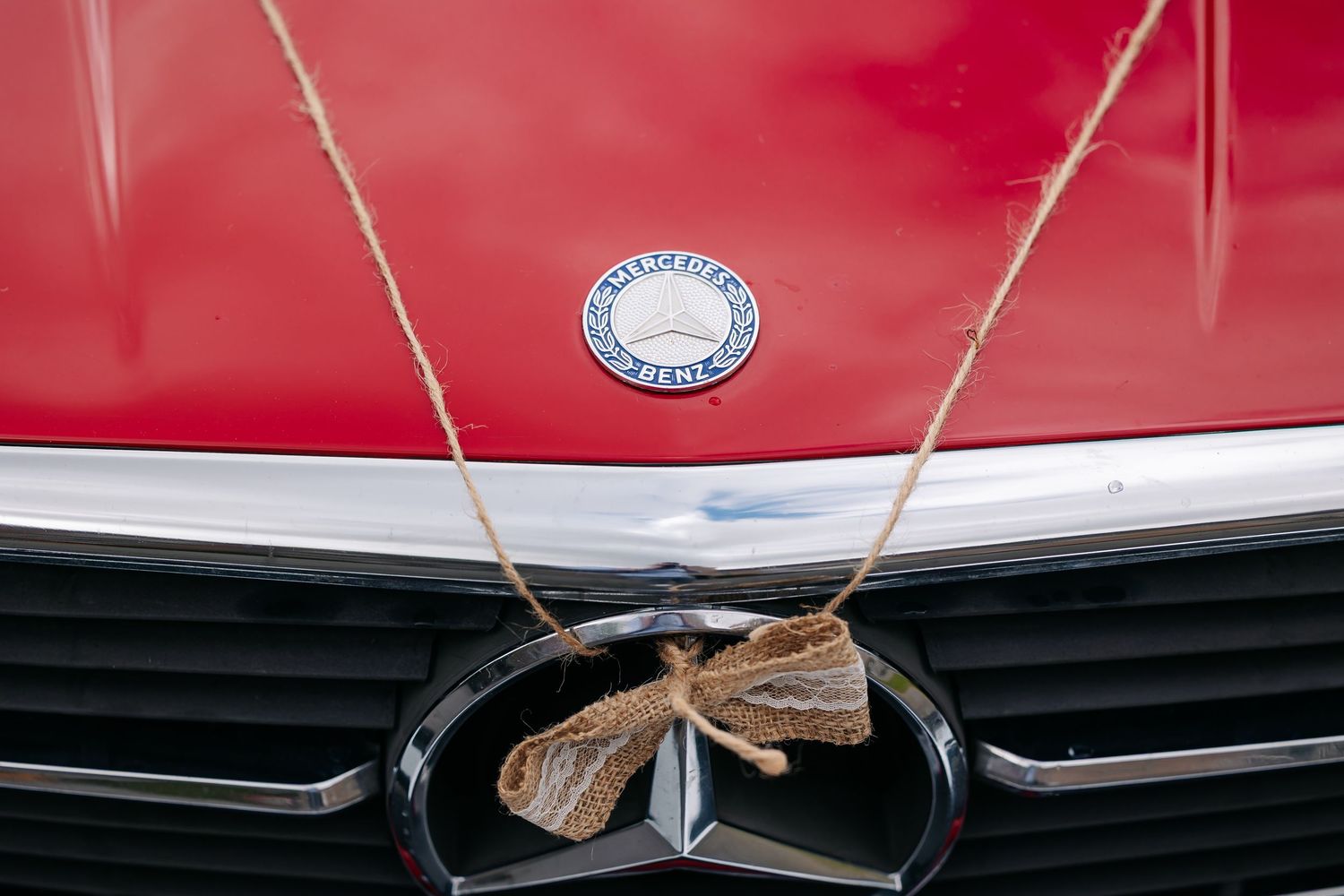 Vintage red Mercedes-Benz car hood ornament with decorative bow and classic logo badge.