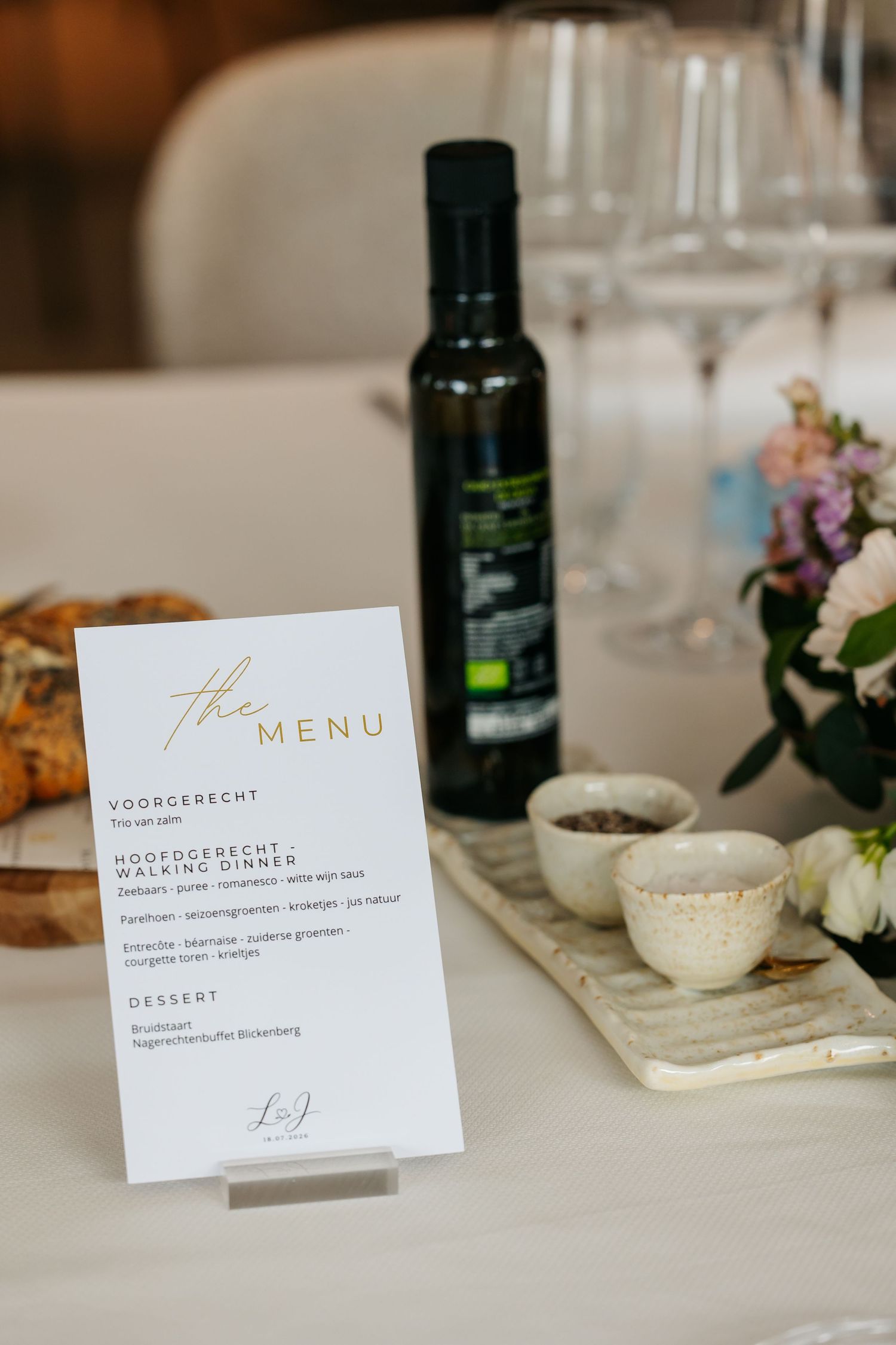 Wedding reception menu card displayed beside olive oil bottle, small ceramic bowls, and floral arrangement.