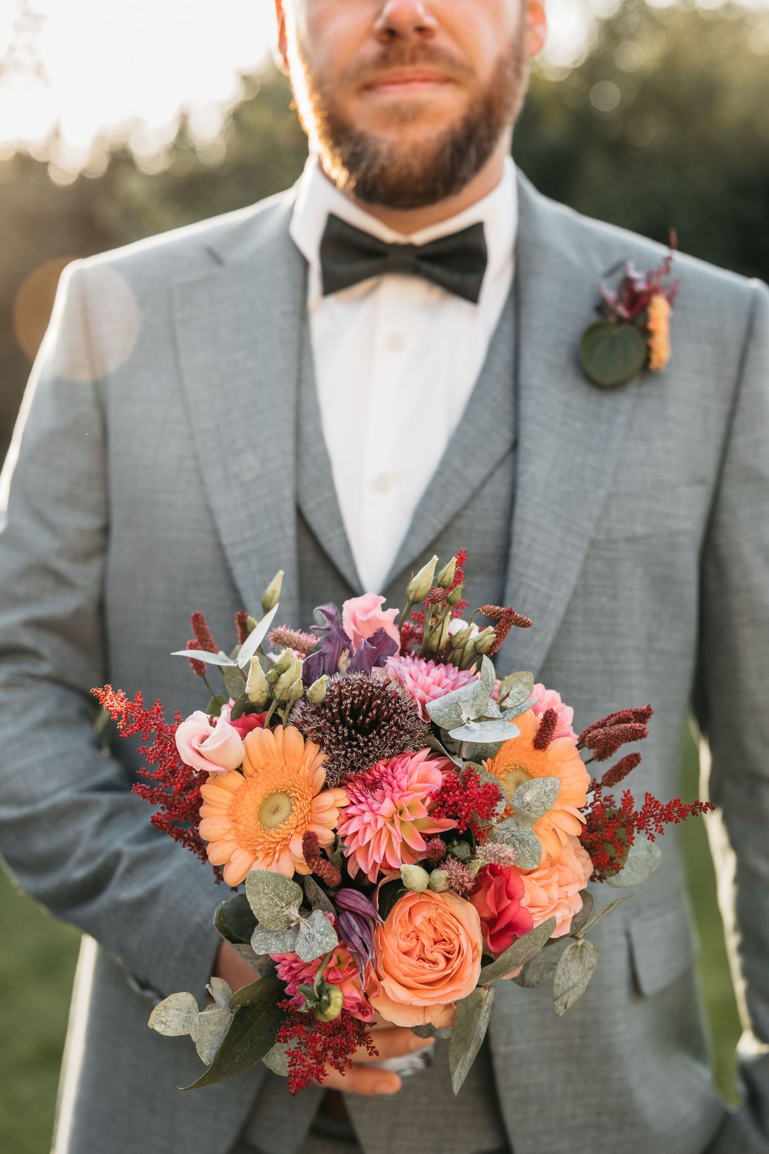 Close-up of groom in grey suit holding a vibrant orange and pink wedding bouquet.