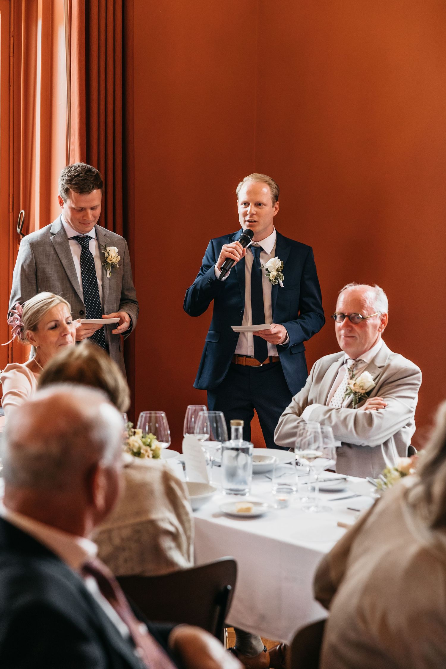 Two groomsmen deliver heartfelt speech at wedding reception dinner with microphone.