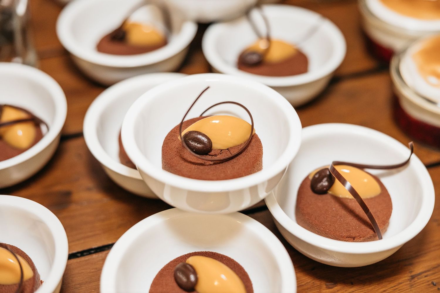 Elegant chocolate desserts with caramel mousse domes garnished with coffee beans served in white dishes at a wedding reception.