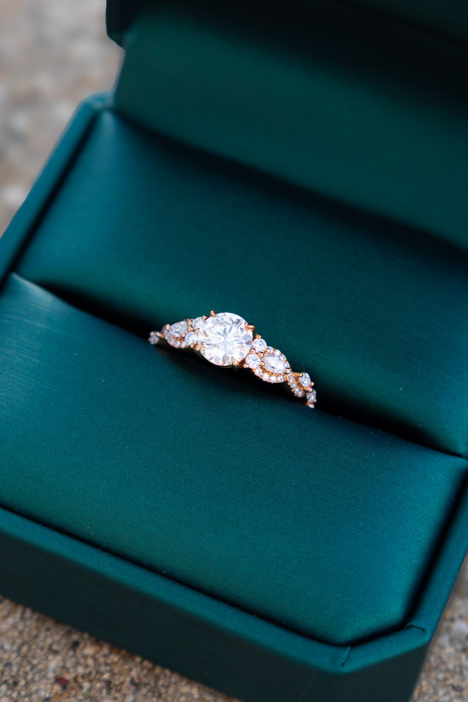 Rose gold engagement ring with round diamond center stone in a green velvet box.