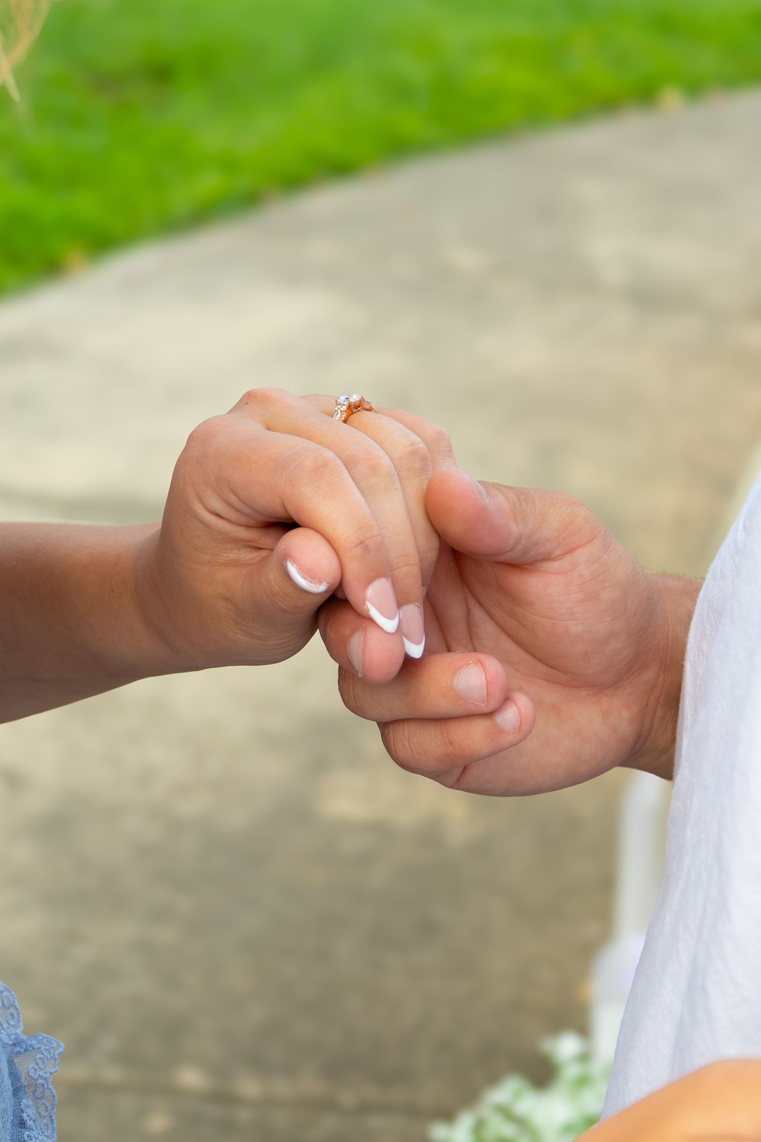 Close-up of couple holding hands outdoors, woman wearing diamond engagement ring with French manicure on wedding day.