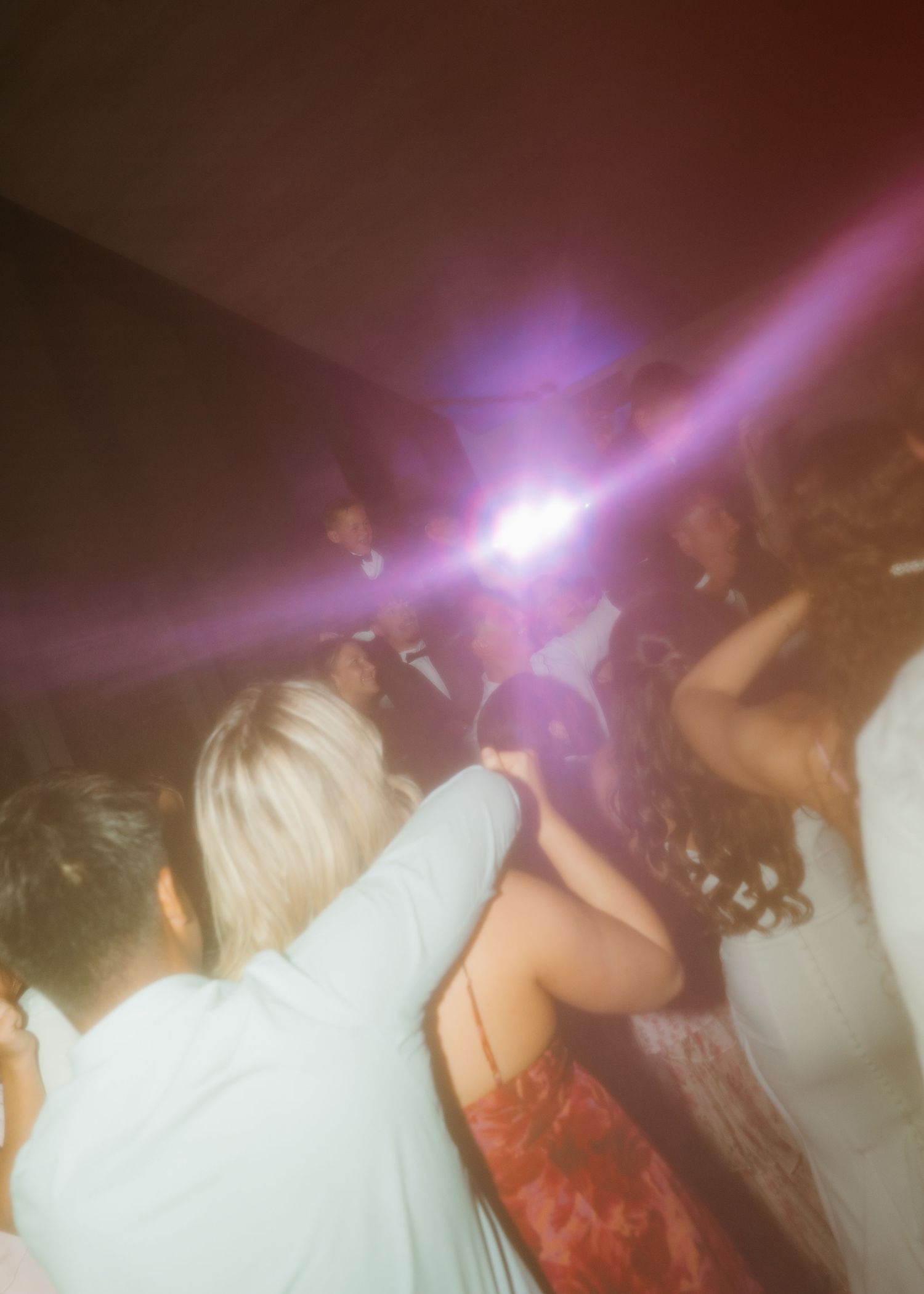Guests dancing at a wedding reception with colorful disco lights illuminating the dance floor.