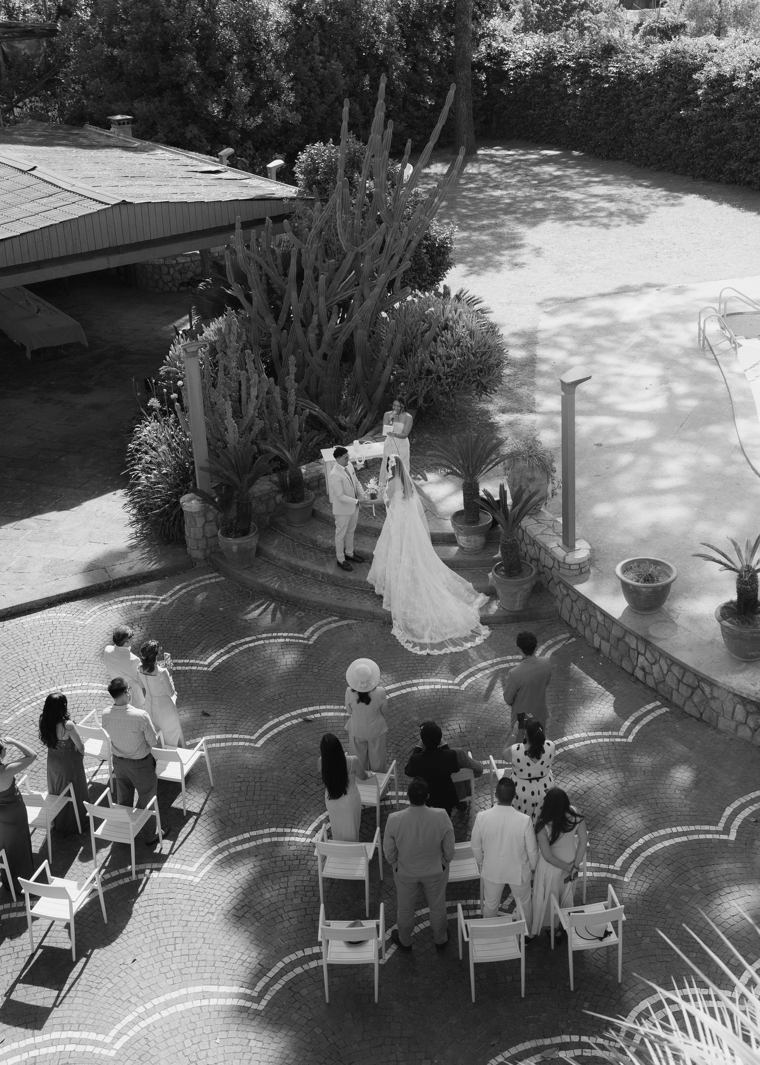 Aerial black and white view of an intimate outdoor wedding ceremony on a mosaic patio with cacti.