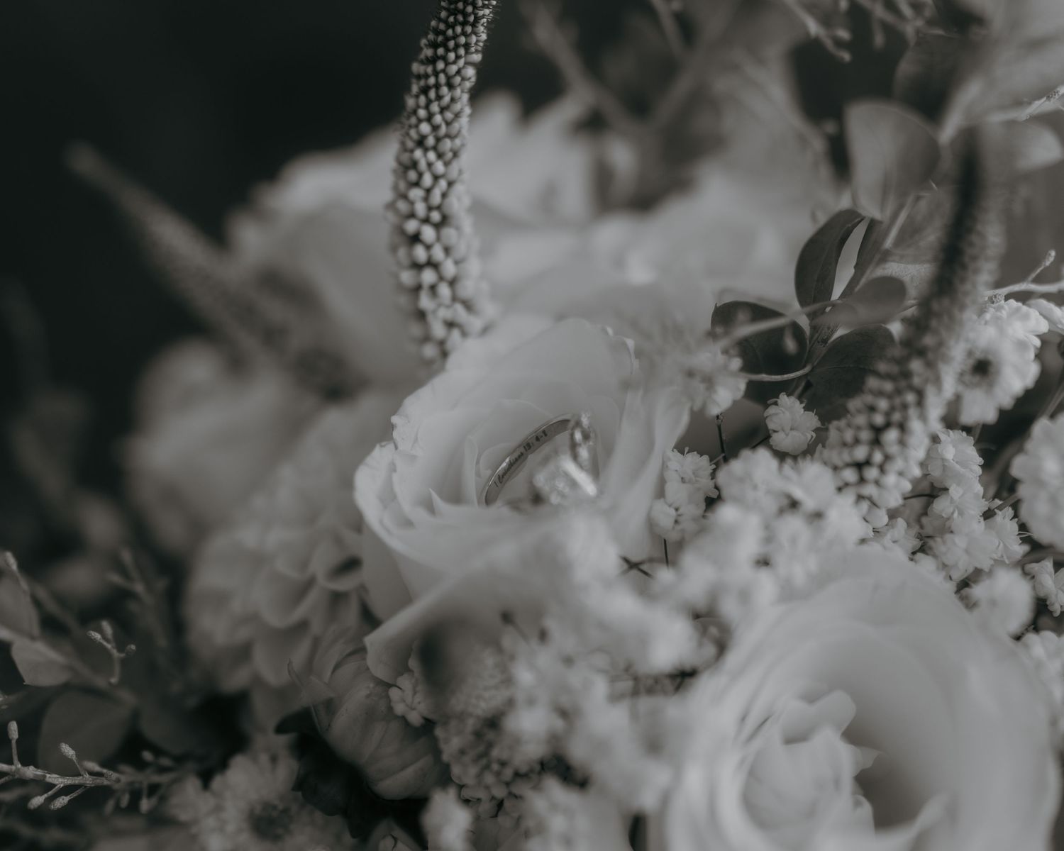 Black and white wedding bouquet with roses and wildflowers, featuring a delicate ring nestled among the blooms.