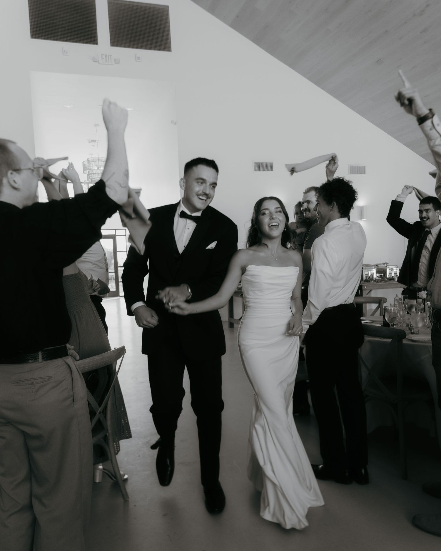 Black and white photo of a smiling bride and groom walking through cheering guests at their wedding reception.