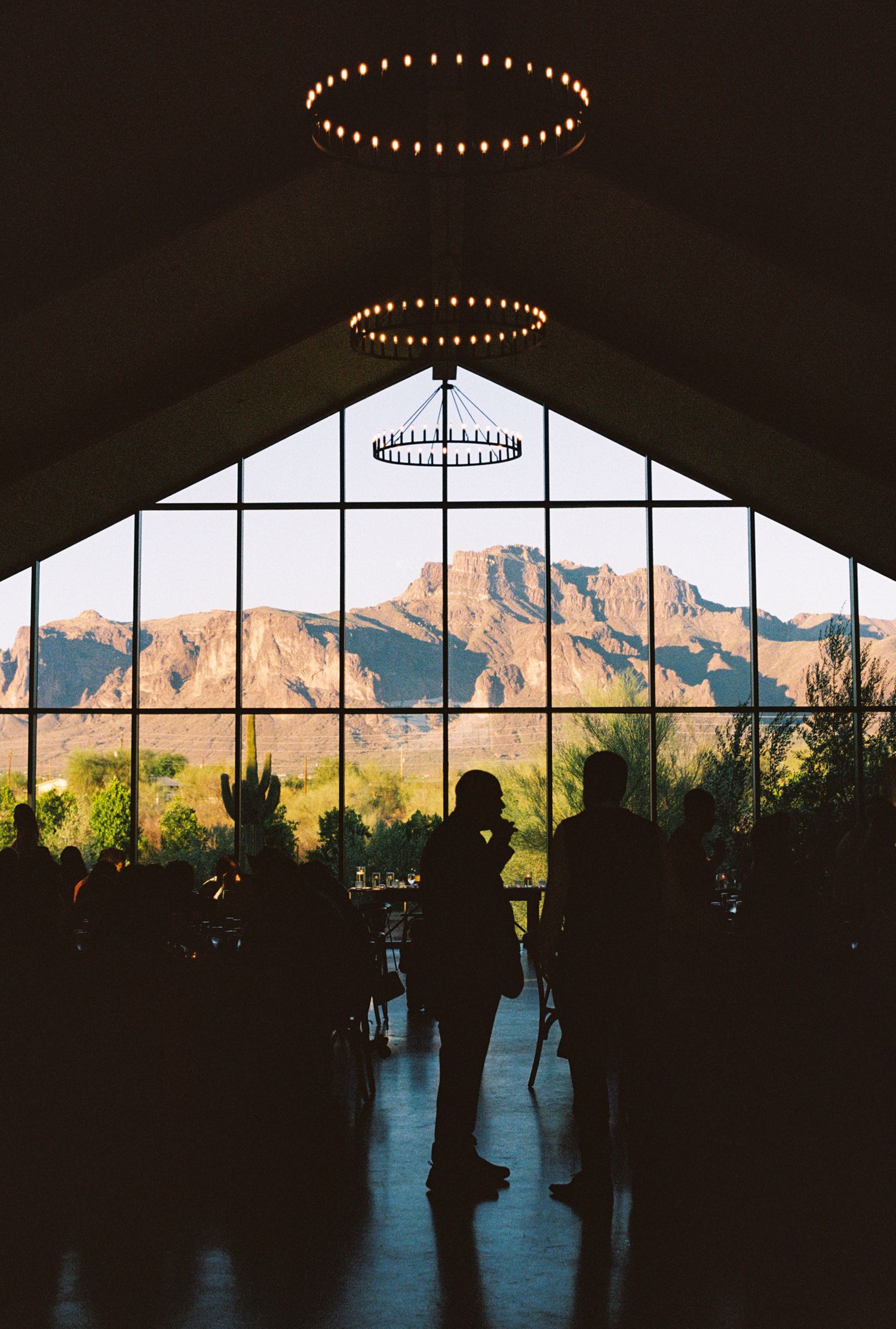 Silhouettes of guests inside a venue with floor-to-ceiling windows overlooking Arizona's Superstition Mountains.