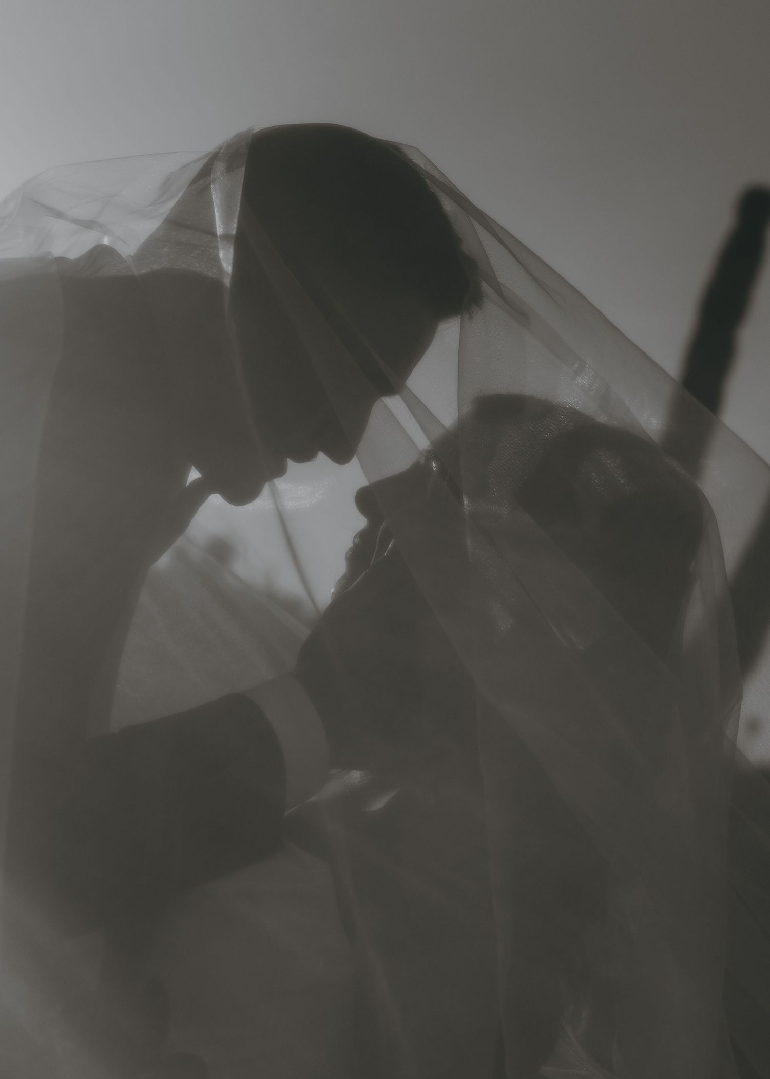 Romantic black and white silhouette of bride and groom sharing an intimate moment under a veil.