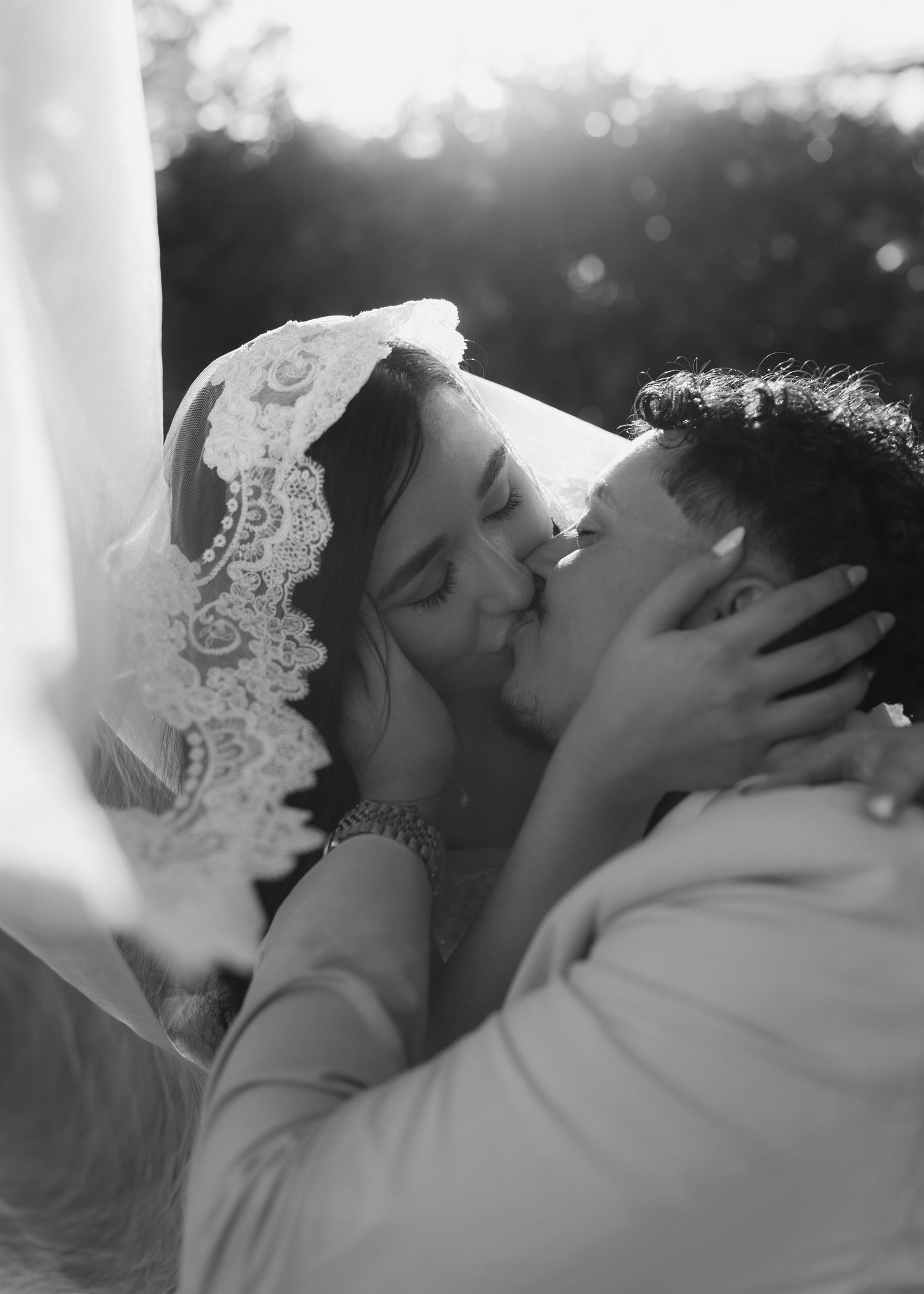 Romantic black and white close-up of bride and groom sharing a kiss under lace wedding veil.