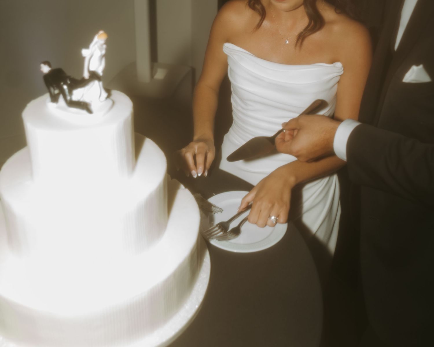 Bride and groom cutting a three-tier white wedding cake topped with bride and groom figurines.