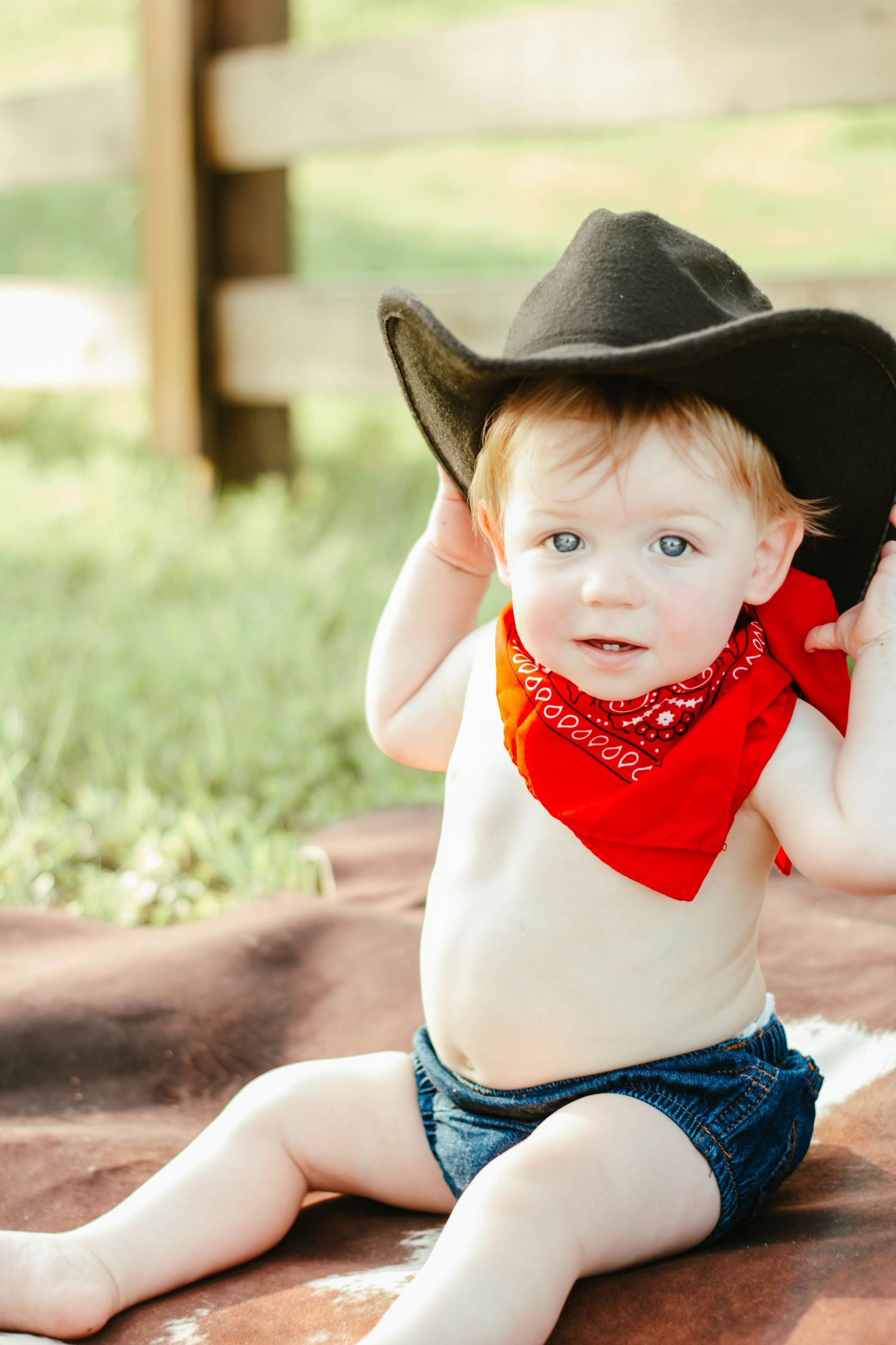 Baby wearing a cowboy hat and red bandana during a western milestone session.