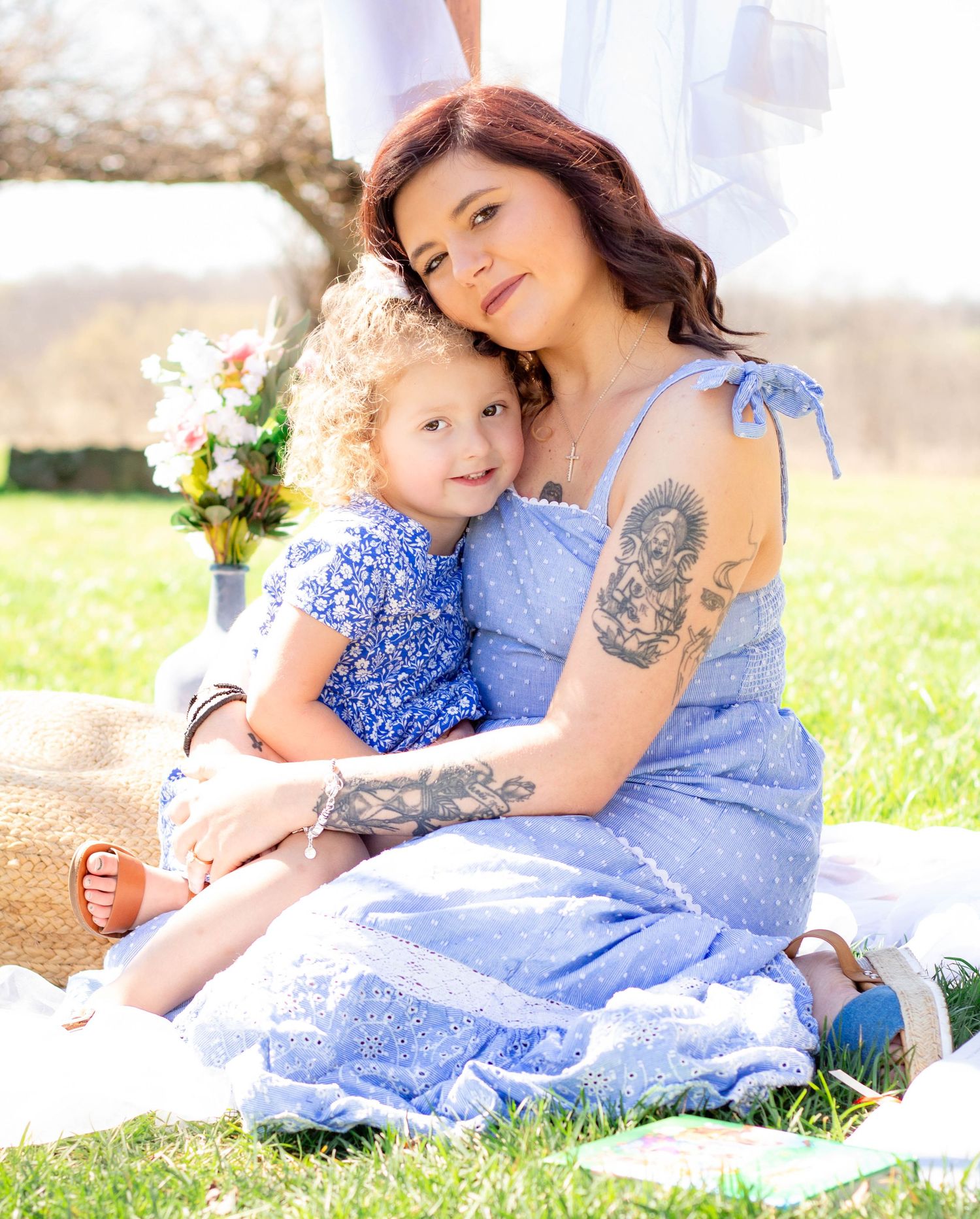 Mother and young daughter sitting together outdoors in coordinating blue dresses