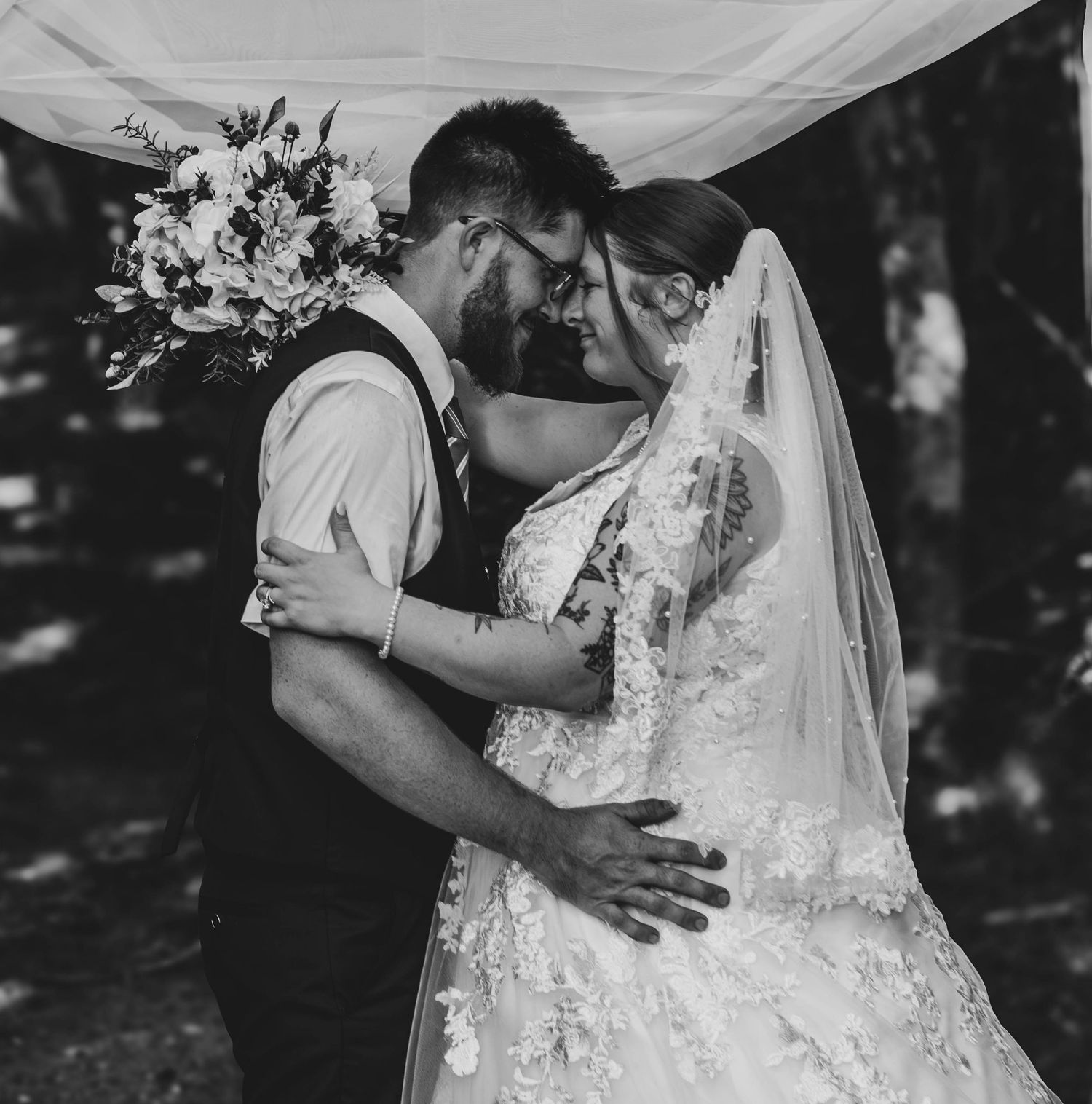 Black-and-white portrait of a bride and groom kissing beneath her veil.