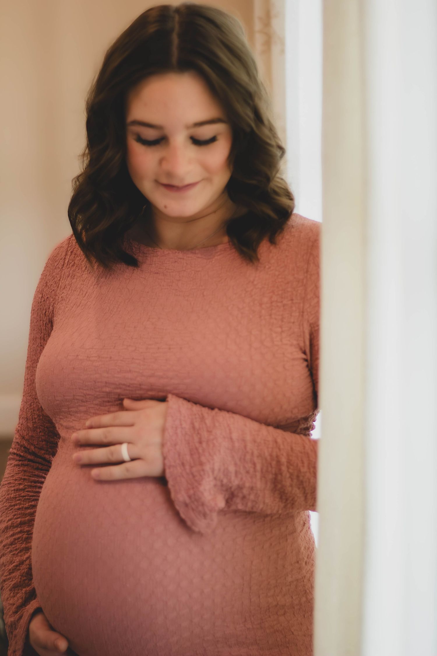 Expectant mother cradling her baby bump during an indoor maternity session.