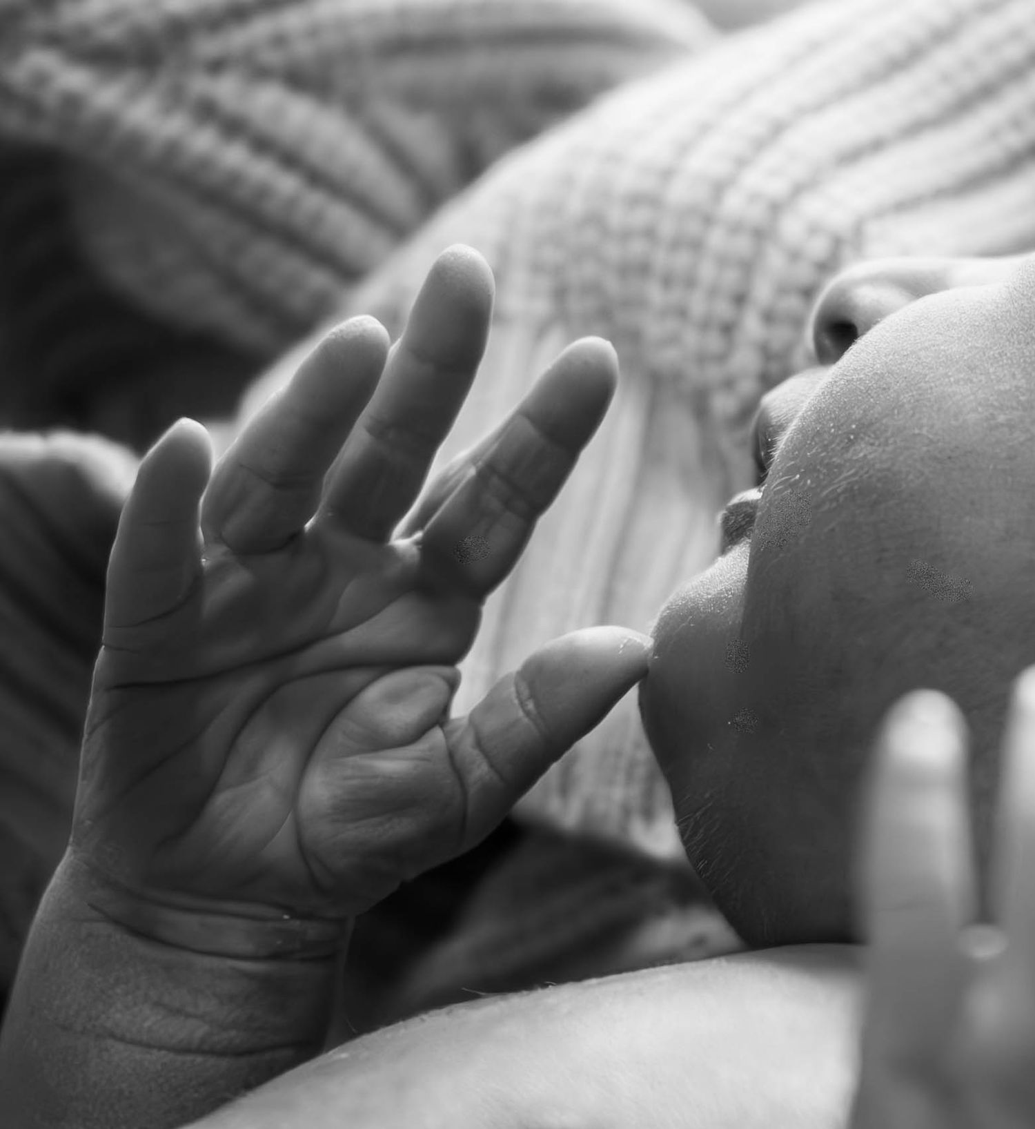 Black-and-white close-up of a newborn baby holding an adult’s finger.