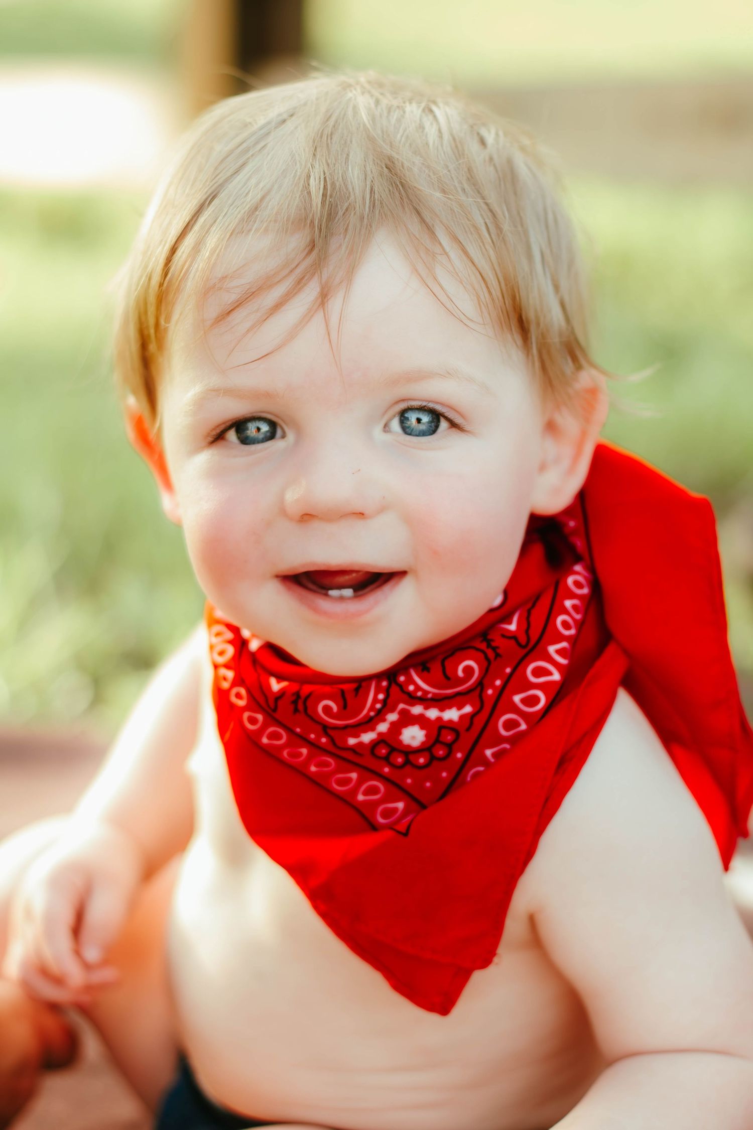 Close-up milestone portrait of a smiling baby wearing a red bandana.