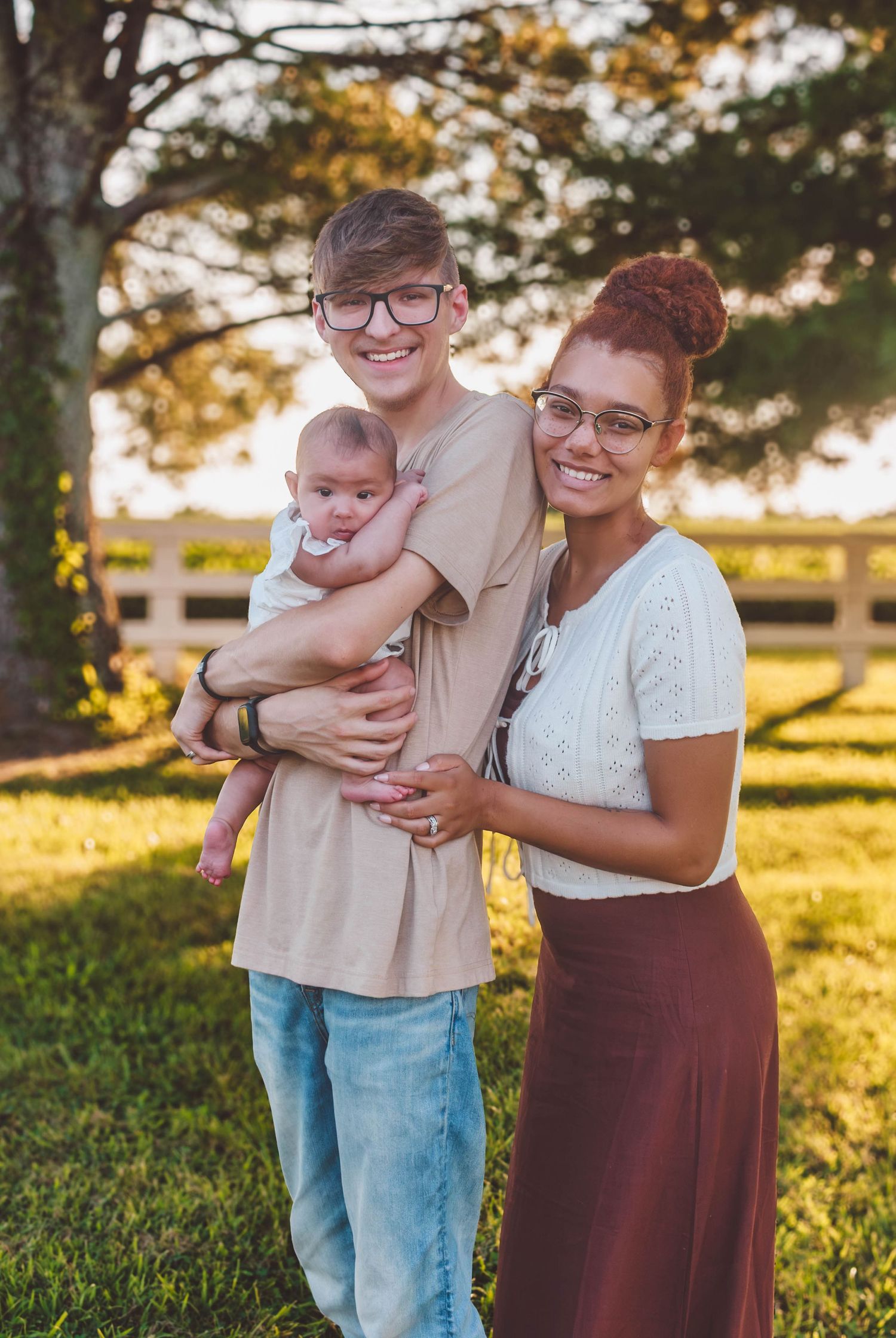 Parents posing outdoors with their newborn baby at sunset
