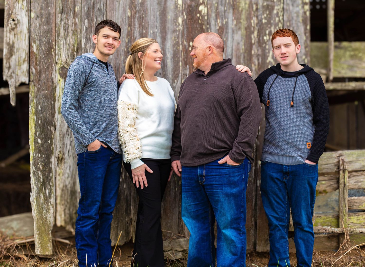 Family of four posing together in front of a rustic wooden barn
