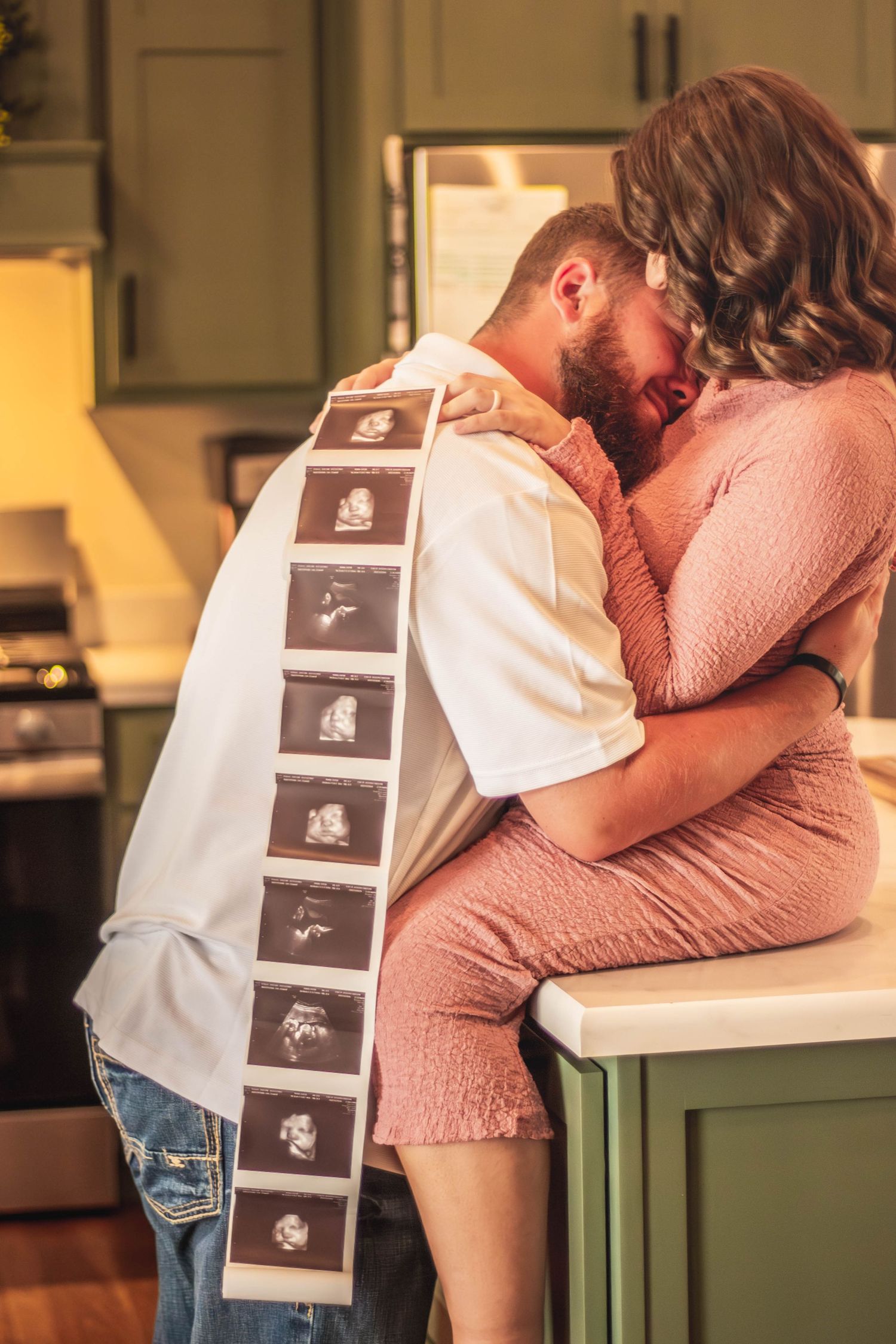 Expecting couple kissing while displaying ultrasound photos during a maternity session.