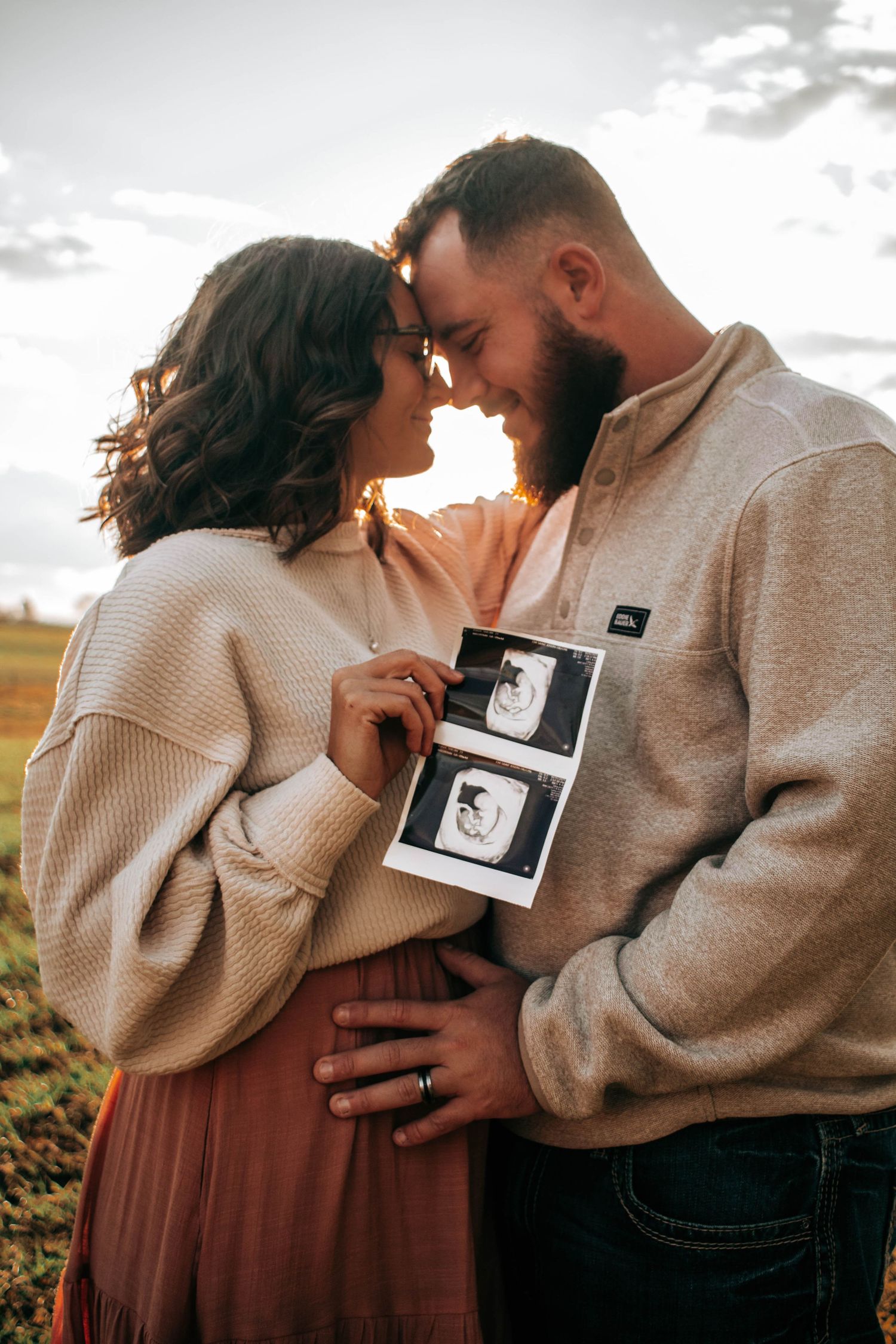 Expecting couple touching foreheads while displaying ultrasound photos.