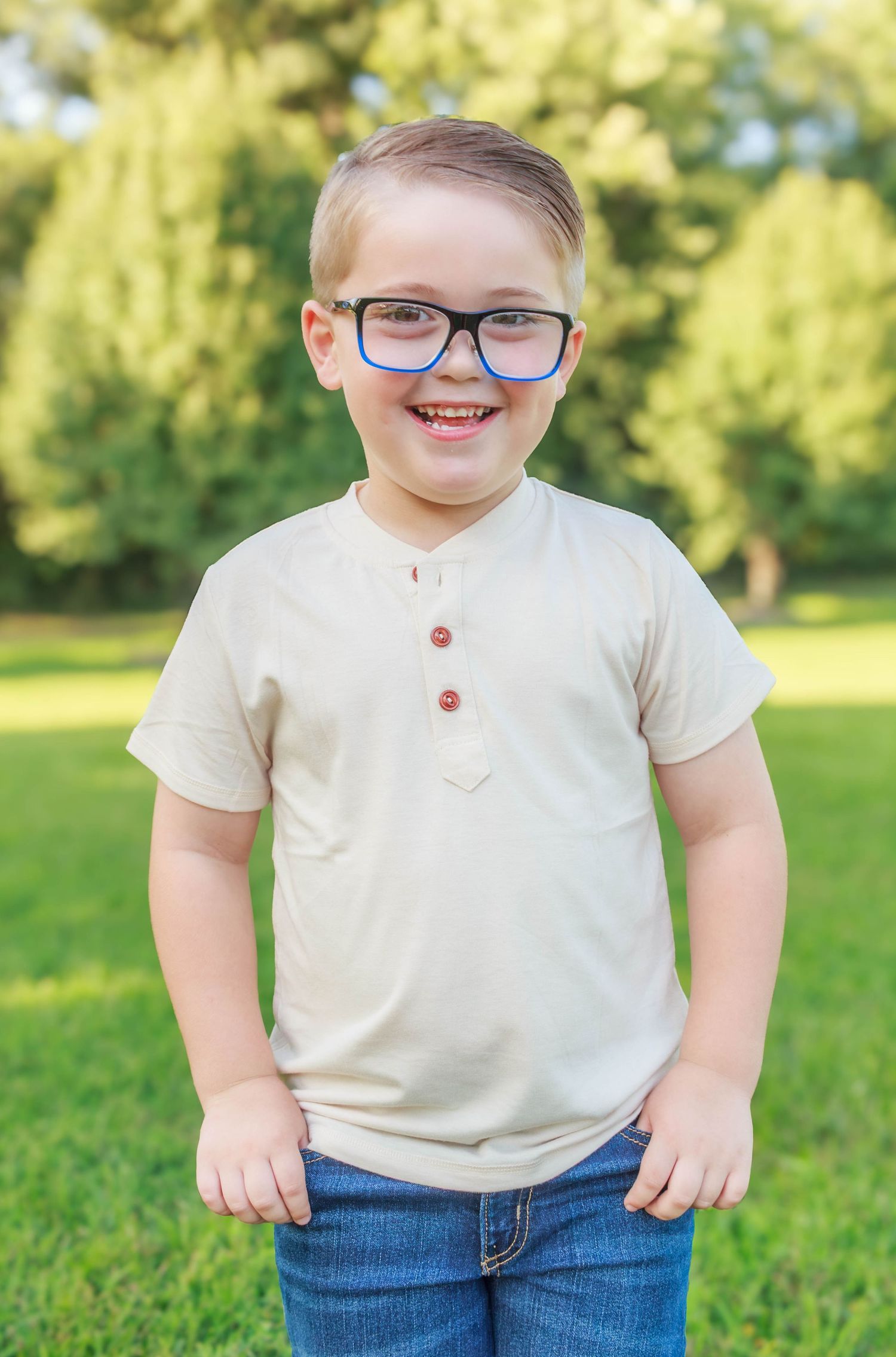 Young boy smiling for an outdoor portrait in a grassy park