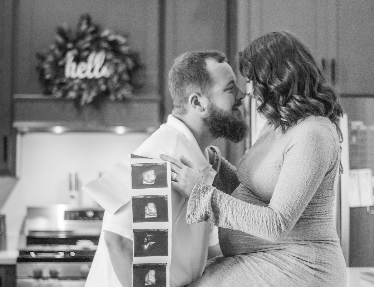 Black-and-white candid of expecting parents embracing with ultrasound photos.