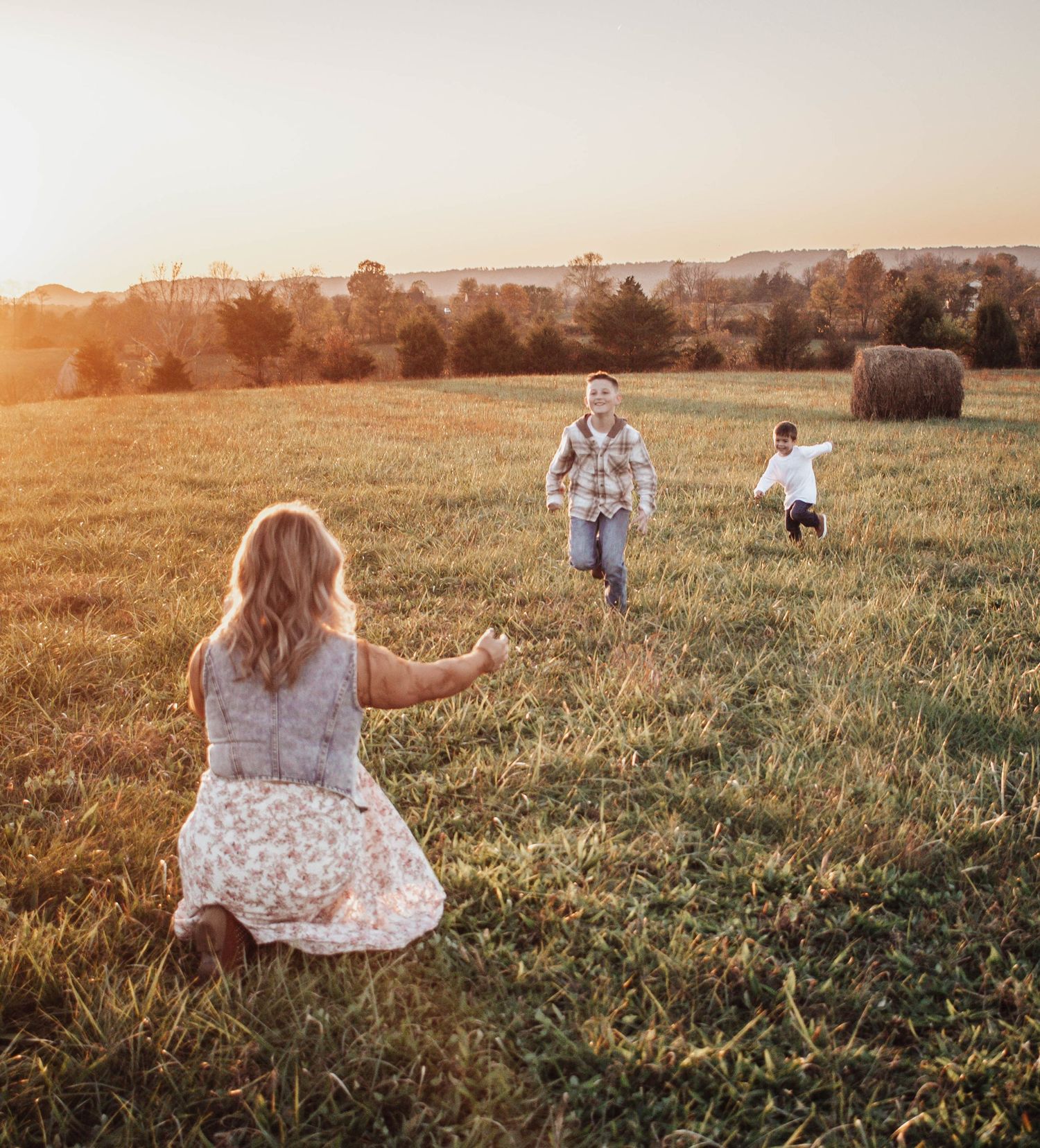Children running toward their mother in a field during a golden-hour family photography session