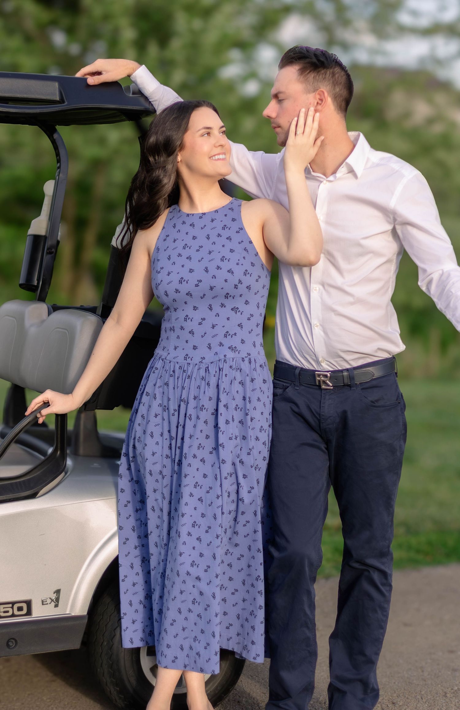 Couple laughing together beside a golf cart outdoors.