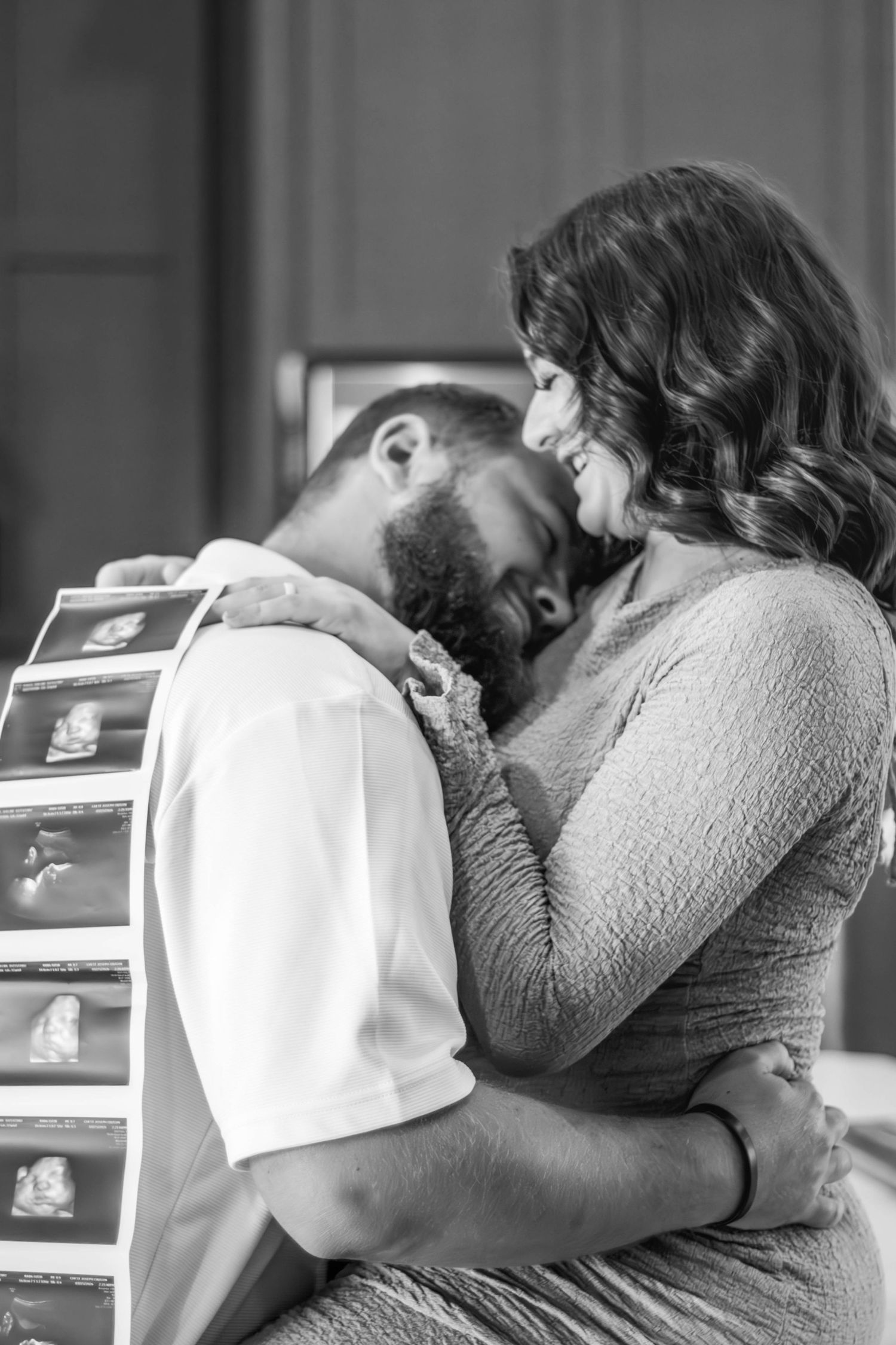 Black-and-white maternity portrait of an expecting couple sharing a kiss.