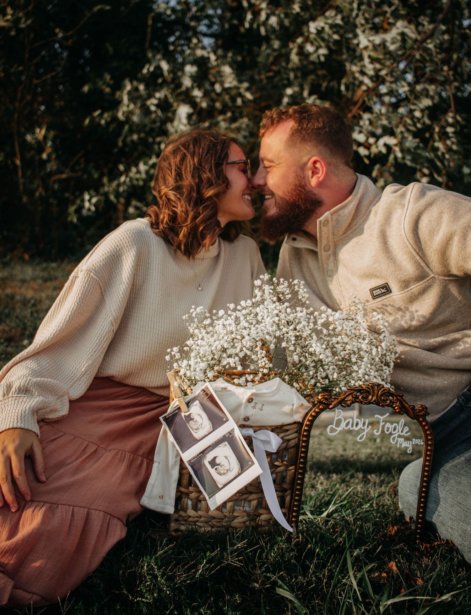 Expecting couple kissing beside their pregnancy announcement during golden hour.