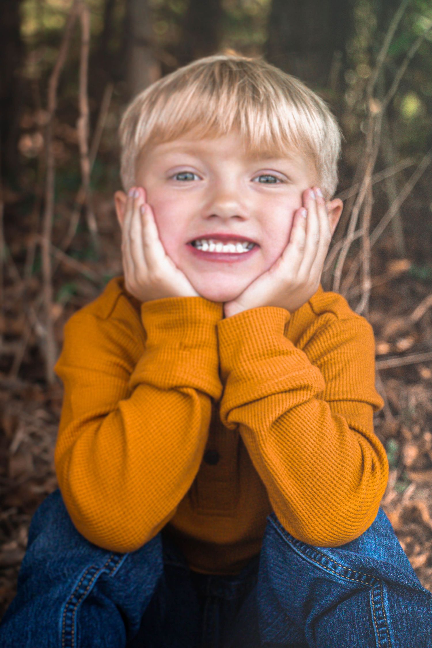 Young boy smiling with his hands on his cheeks during a fall portrait session