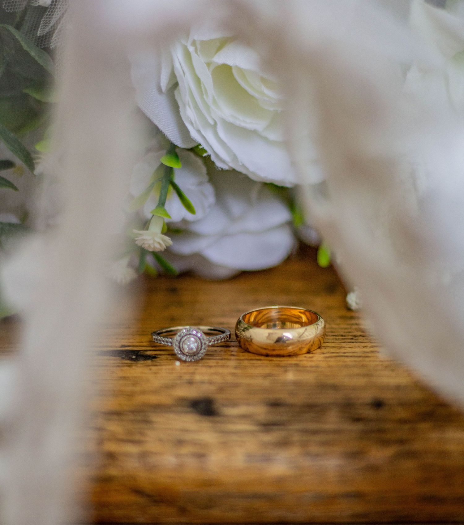 Close-up of wedding rings arranged beside white flowers.