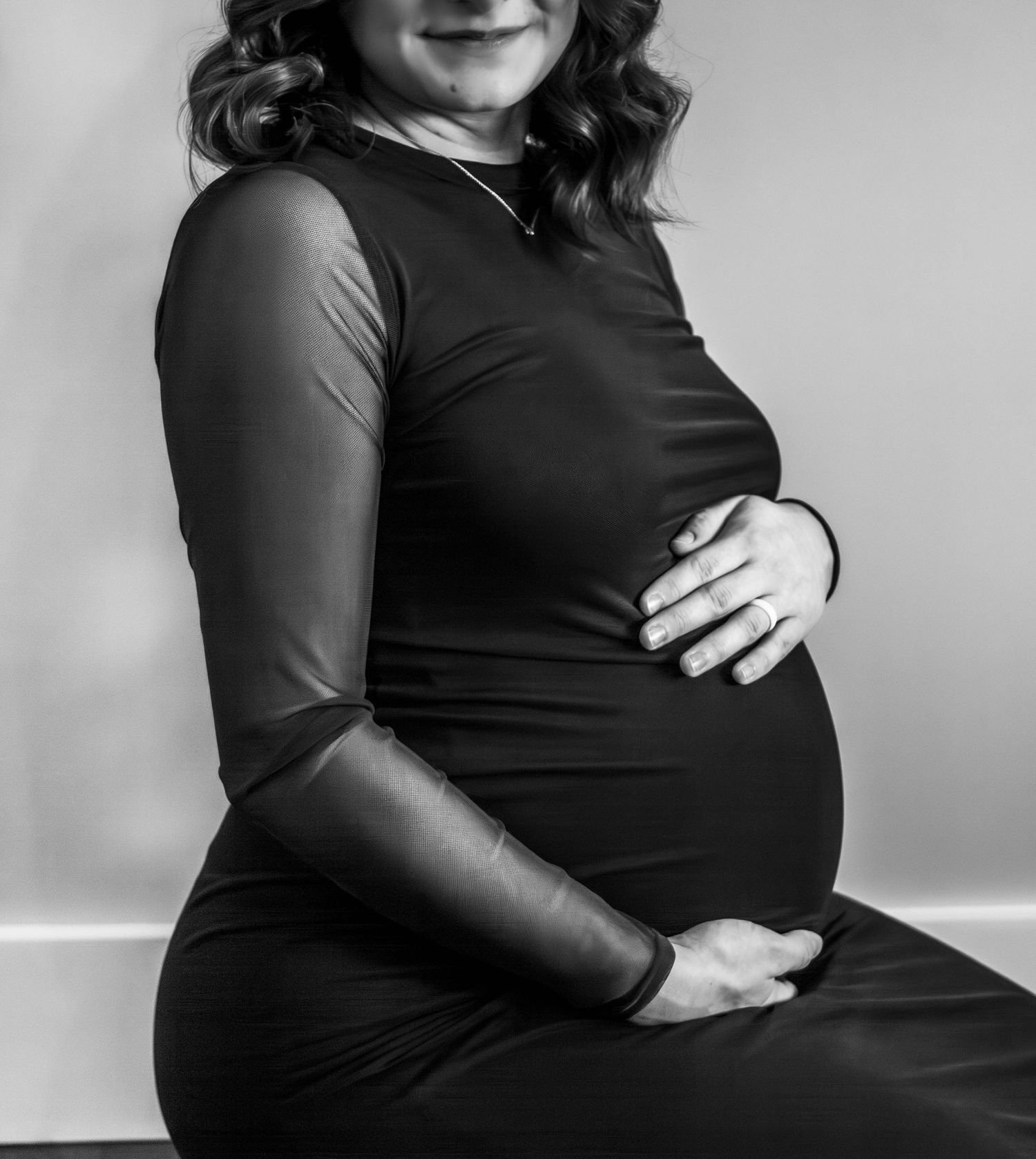 Black-and-white studio maternity portrait of an expectant mother cradling her belly.