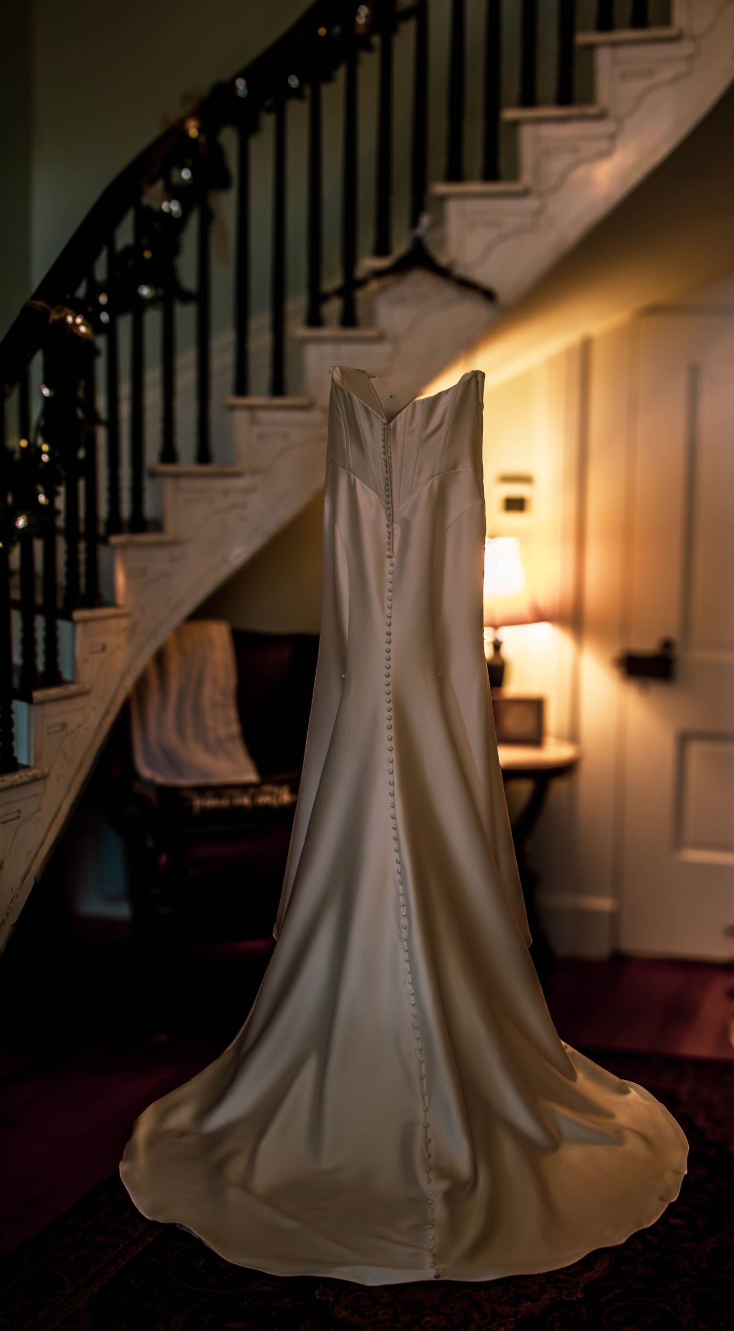 Wedding dress displayed beside a staircase in warm window light.