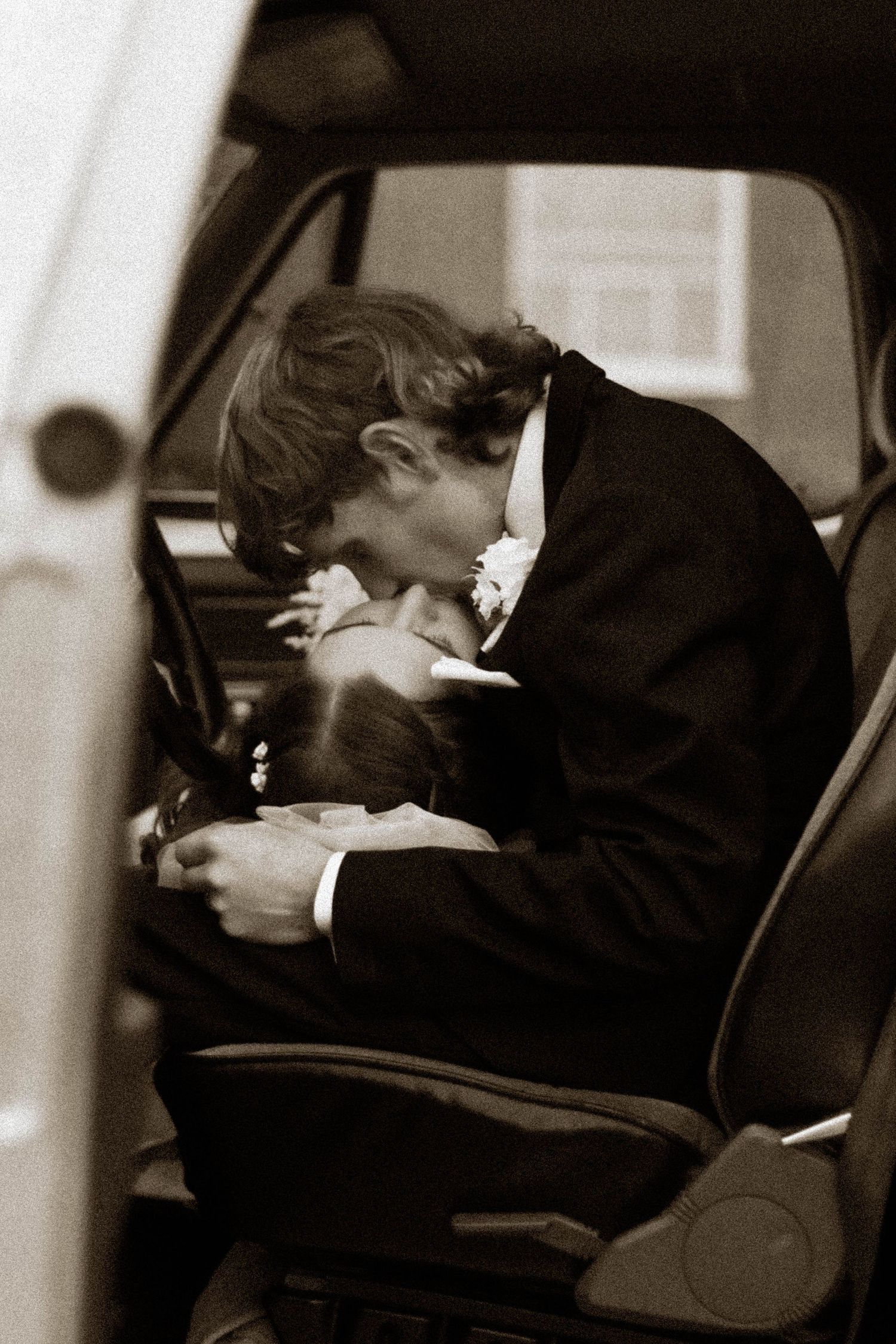 Black-and-white candid portrait of a groom kissing inside a vehicle