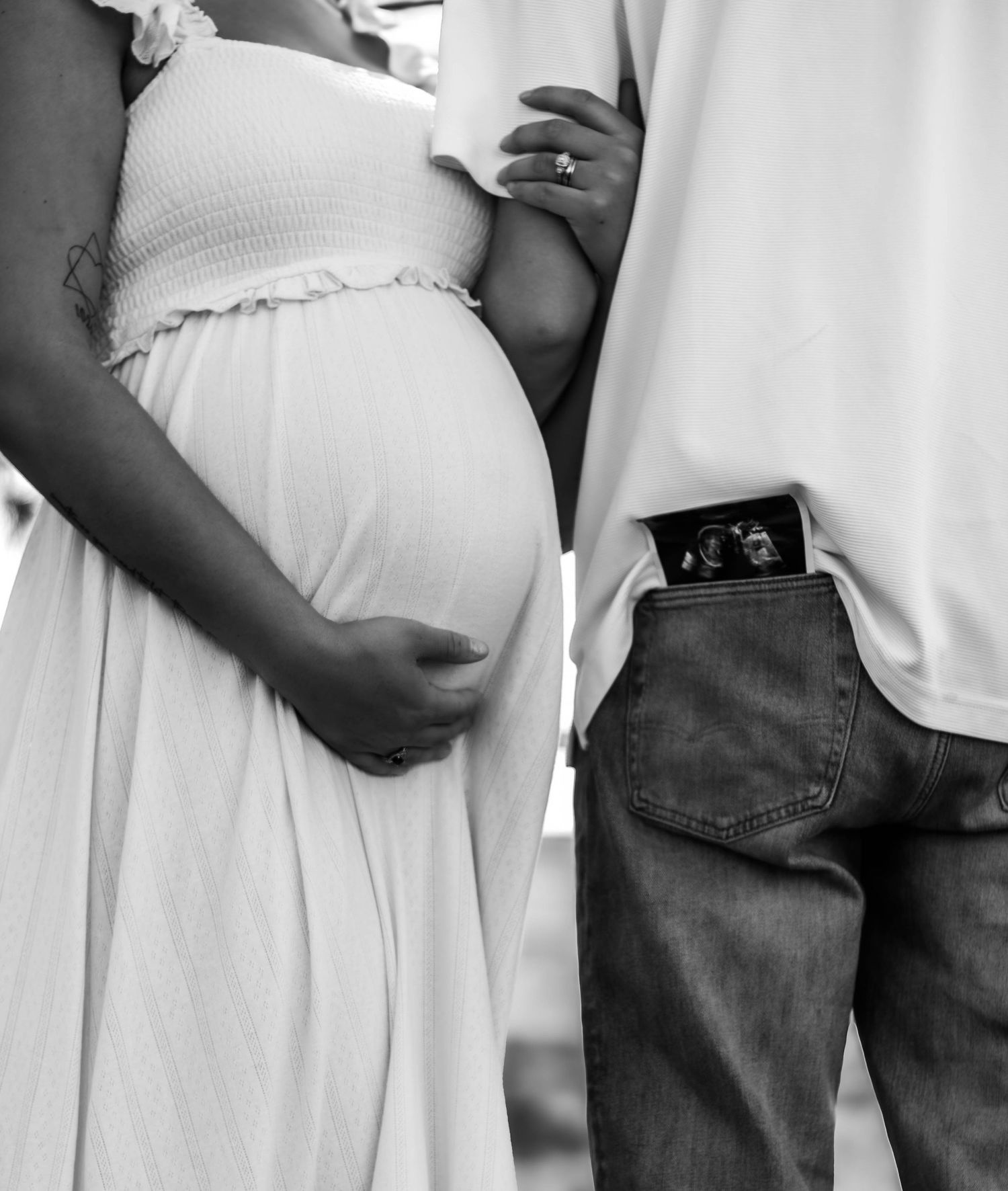 Black-and-white close-up of expecting parents’ hands resting on the baby bump.
