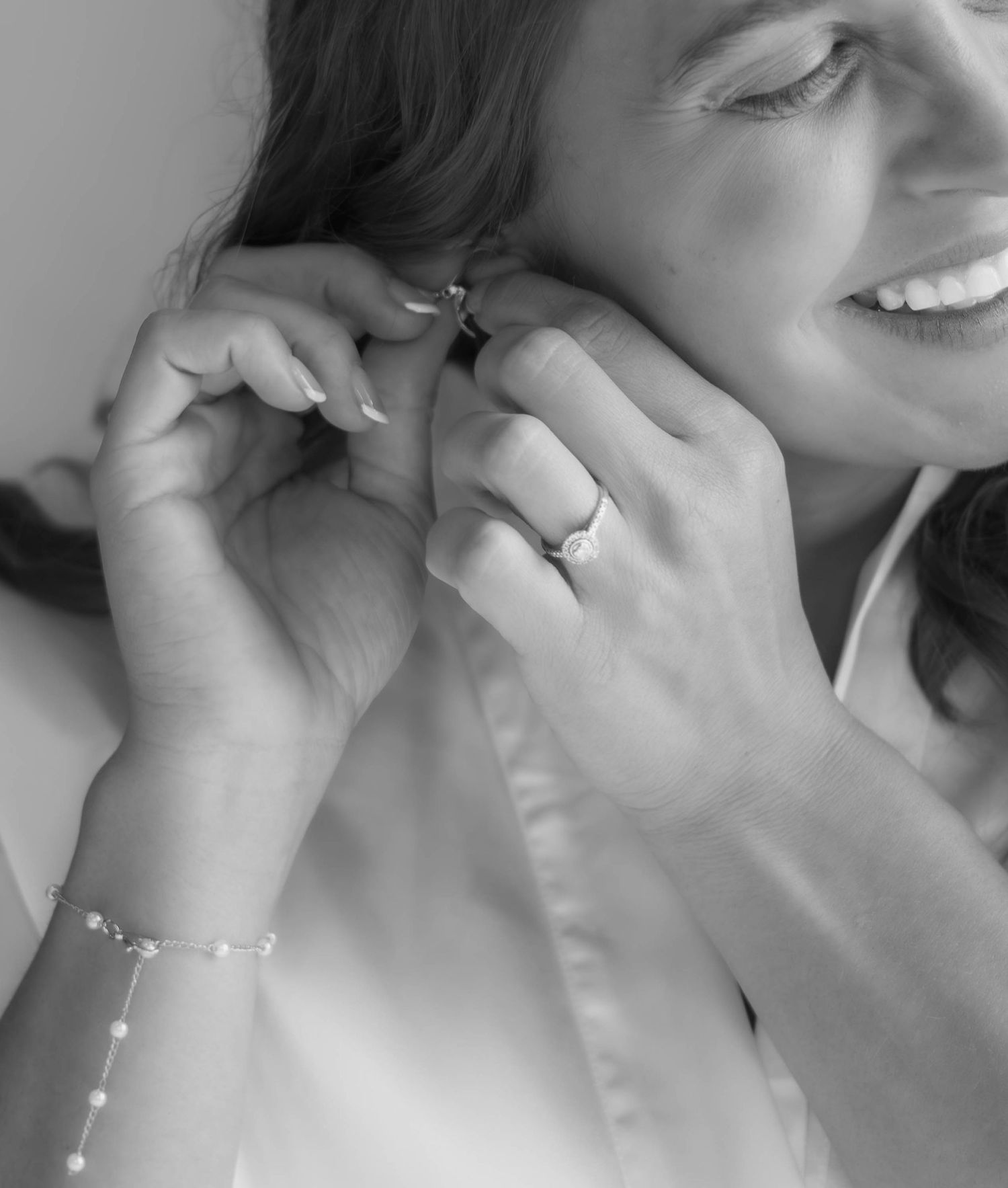 Black-and-white close-up of a bride putting on her wedding earrings.